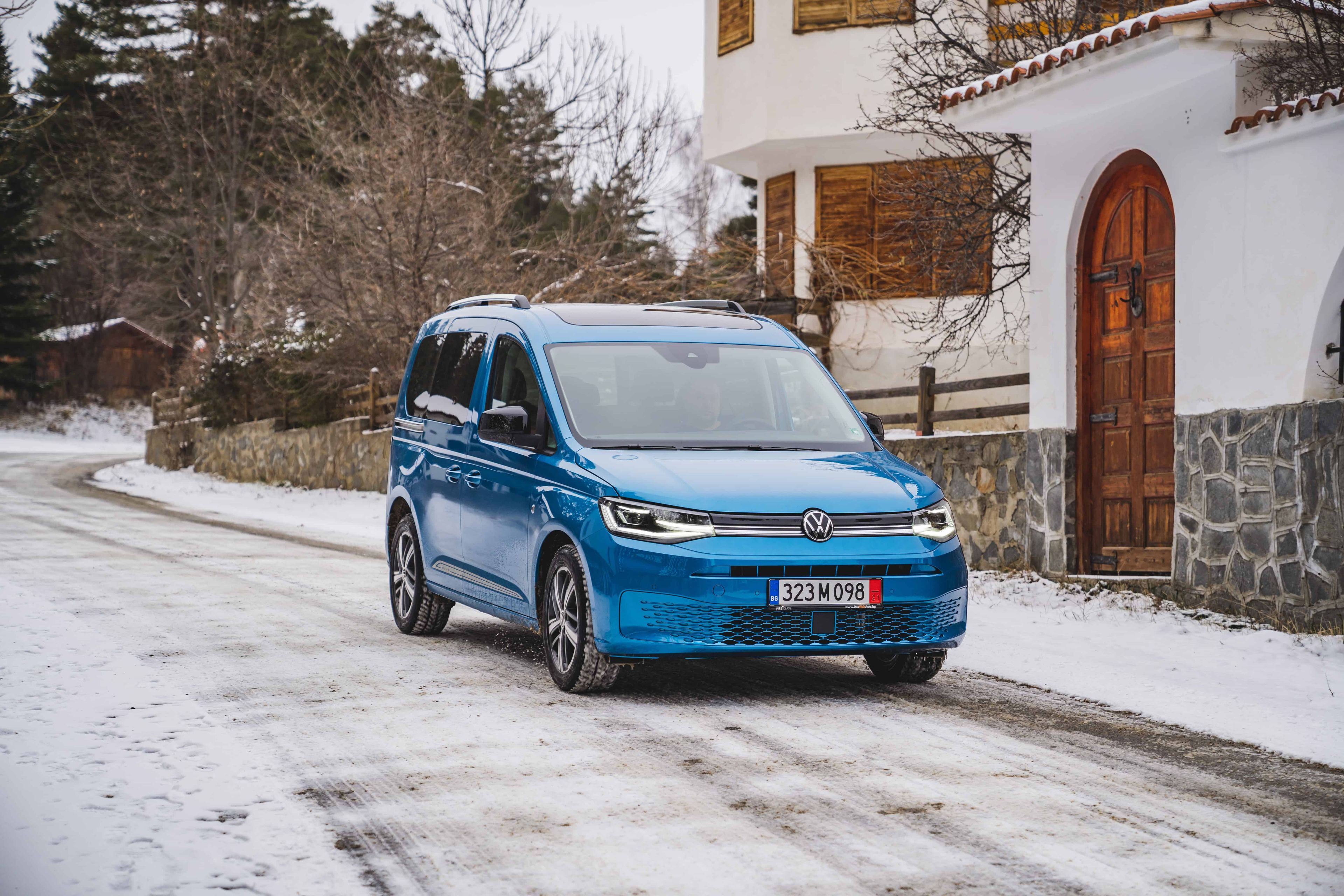 Volkswagen Caddy – стил и комфорт през всяко пътуване Син Volkswagen Caddy на заснежен път пред къща с дървени капаци