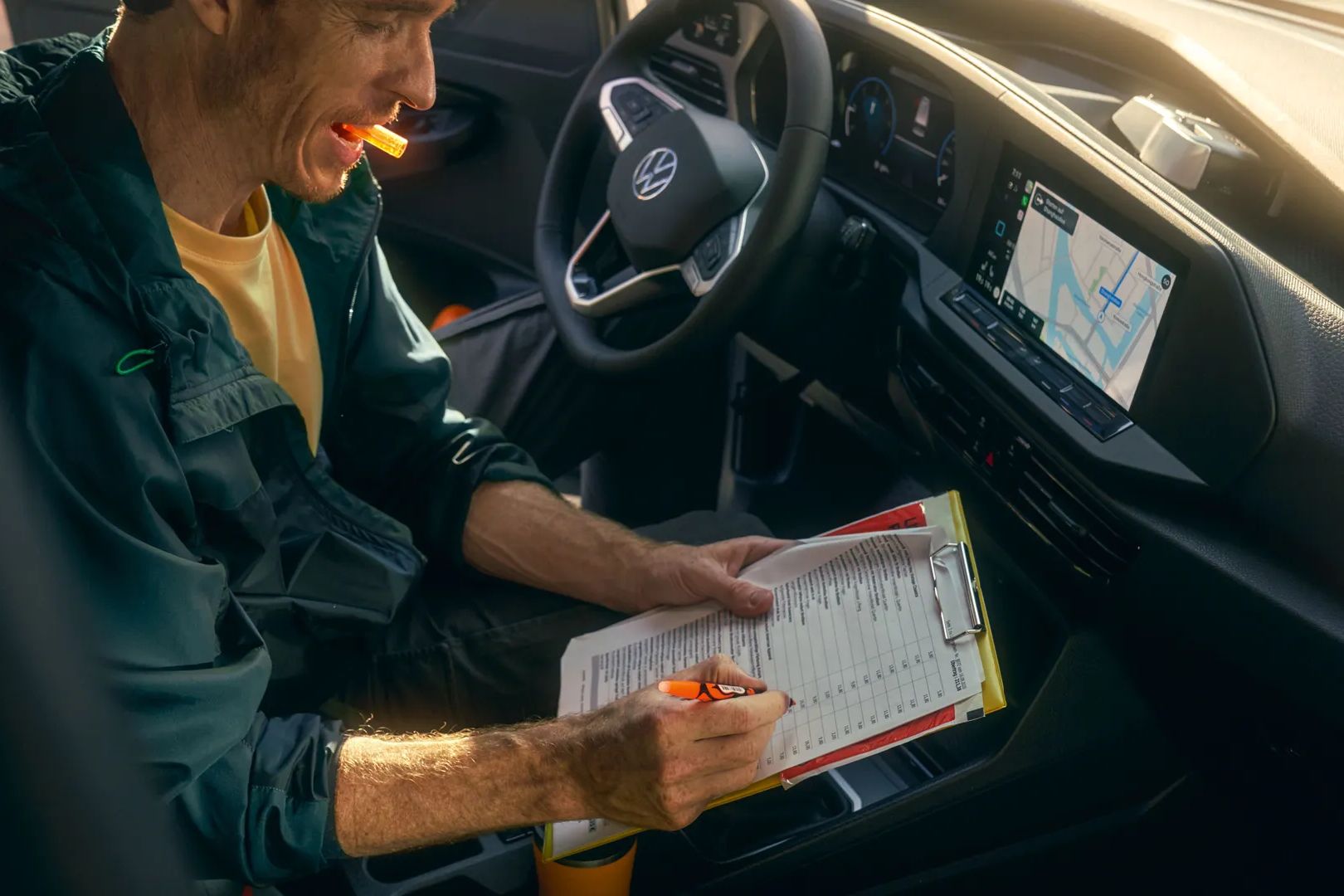Човек попълва формуляр на клипборд с химикалка, докато седи в кола с навигационен екран, показващ карта на таблото.