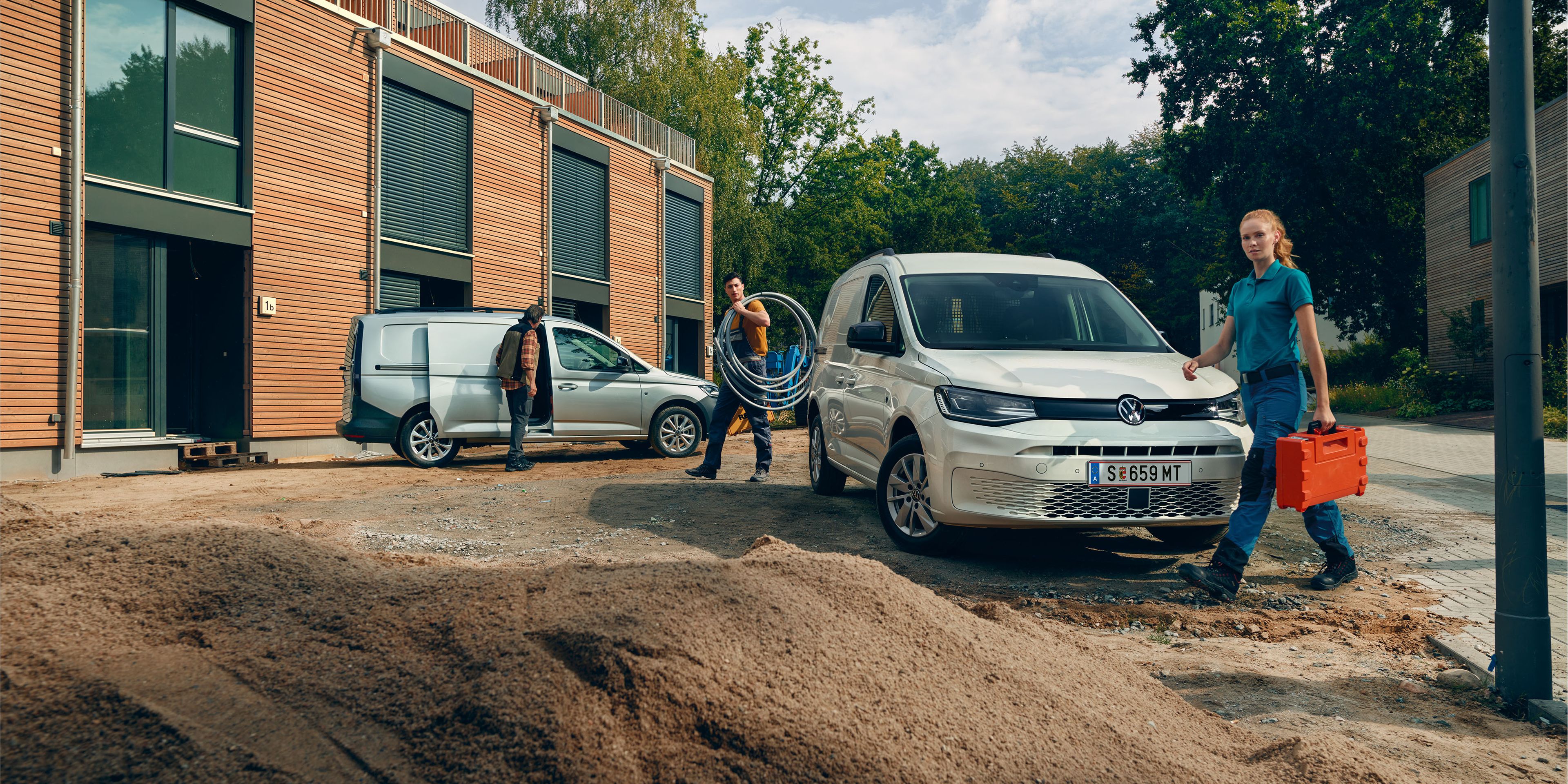 Два товарни автомобила Volkswagen Caddy на строителен обект, с трима професионалисти, носещи инструменти и оборудване.