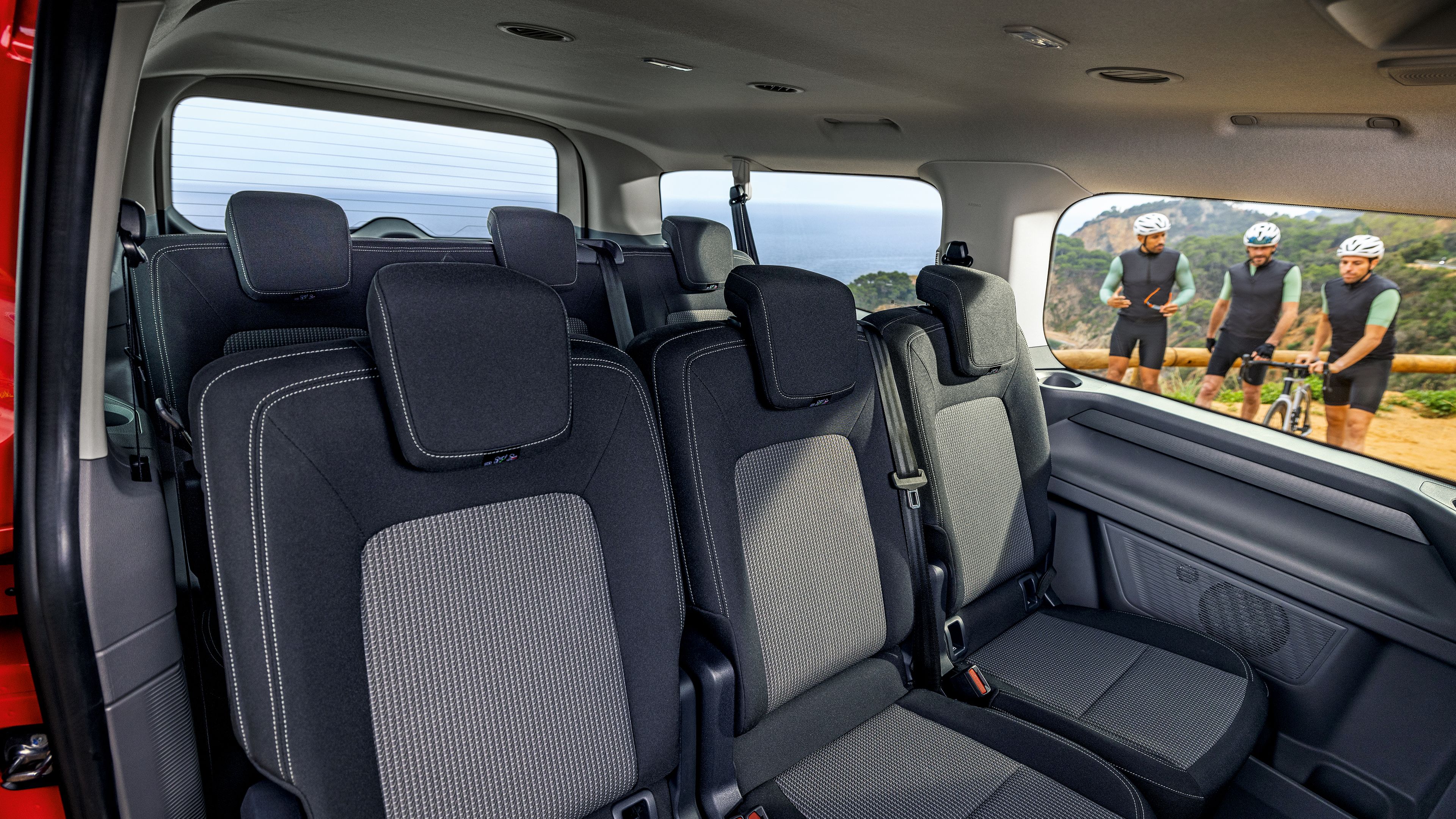 Интериор на Volkswagen Caravelle с три реда седалки и изглед към колоездачи през прозореца