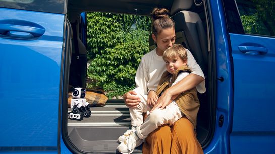Eine Mutter sitzt mit ihrem Sohn im Rahmen einer offenen Schiebetür des neuen VW Multivan T7 2021.