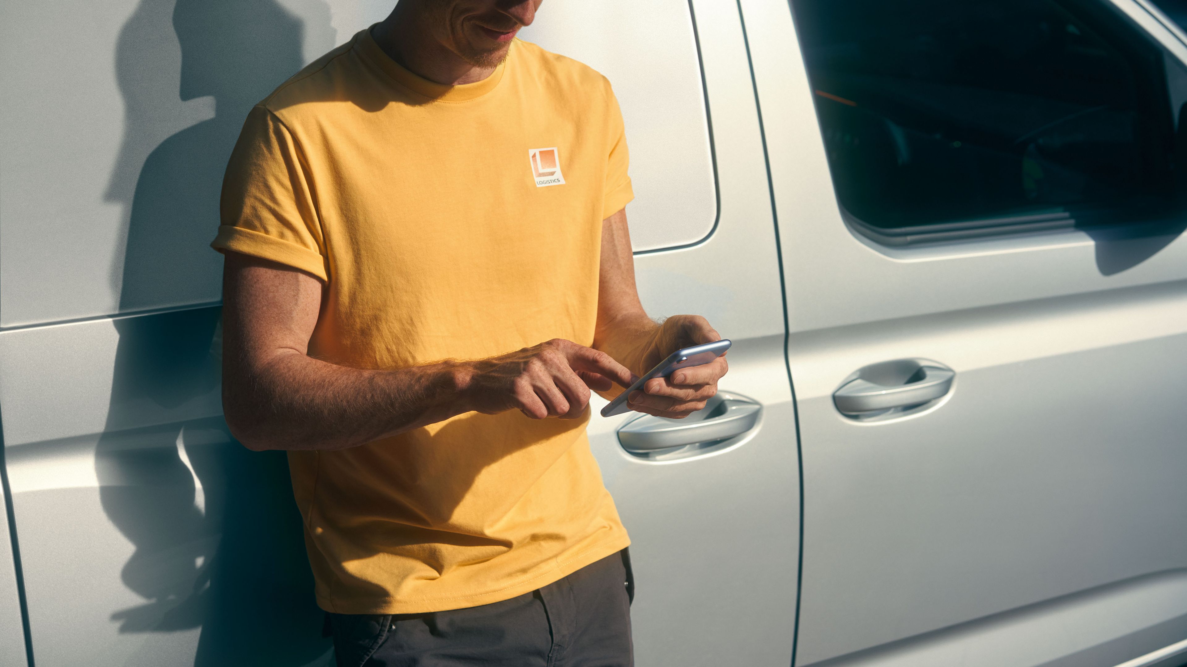 Мъж се е облегнал на VW Caddy Cargo Maxi и използва смартфона си.