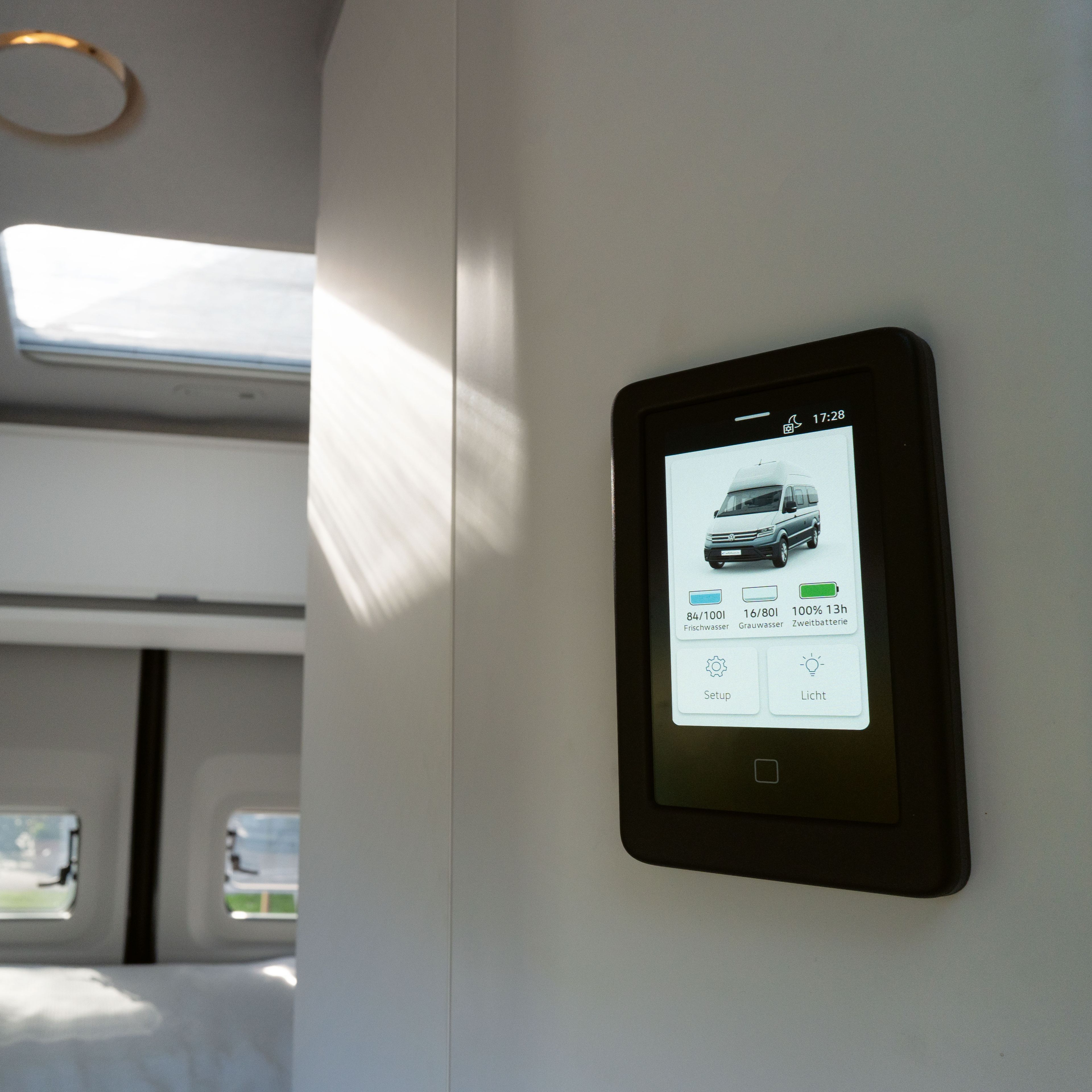 Ein modernes Schlafzimmer in einem Wohnmobil mit einem Touchscreen-Bedienfeld zur Steuerung verschiedener Funktionen. Das Zimmer hat große Fenster und ein Dachfenster, das viel Tageslicht hereinlässt. Dieser Raum scheint luftig und geräumig zu sein.
