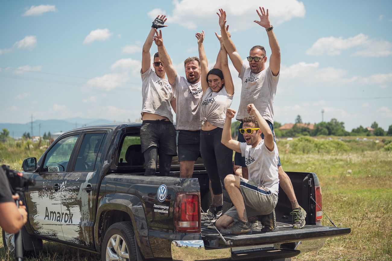 Екип, празнуващ върху Volkswagen Amarok след офроуд приключение Група хора, стоящи в товарното отделение на Volkswagen Amarok, празнуват с вдигнати ръце след офроуд събитие