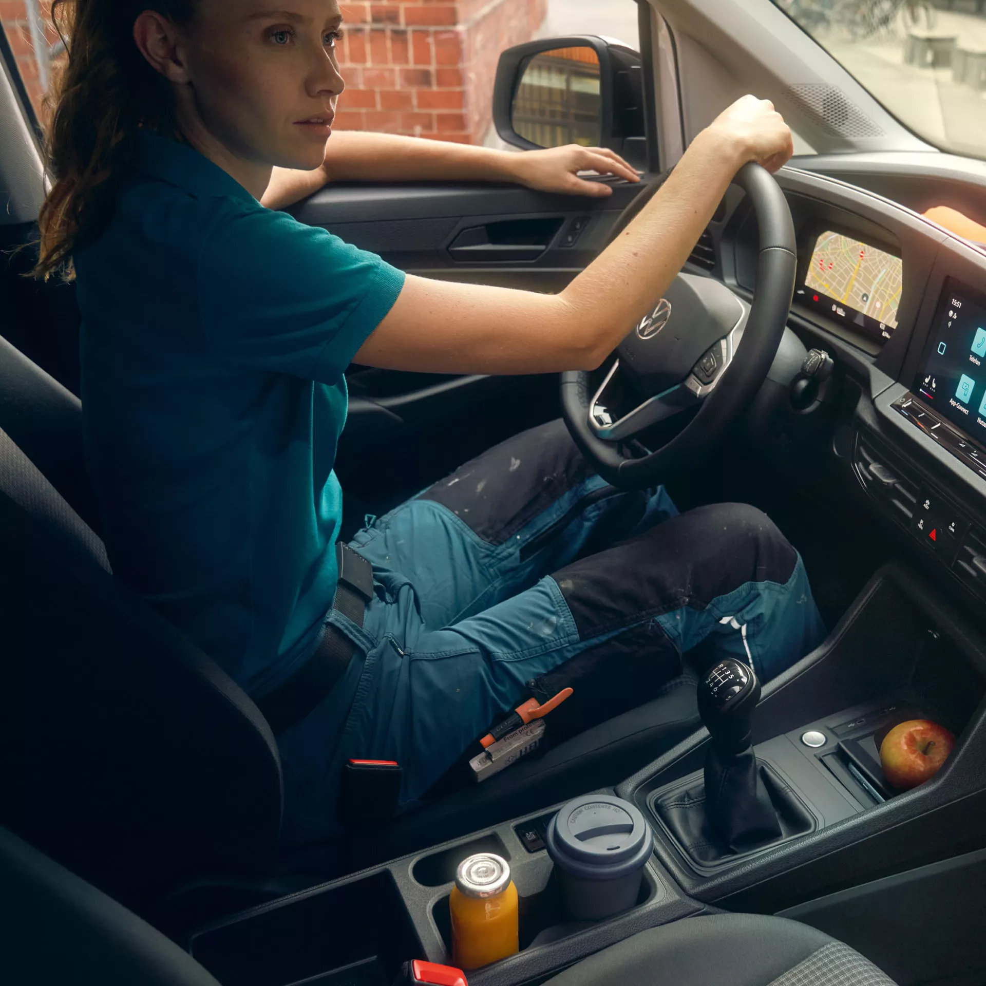 Жена в работно облекло управлява автомобил Volkswagen с активирана навигация, показана на цифровия дисплей, с инструменти в централната конзола.