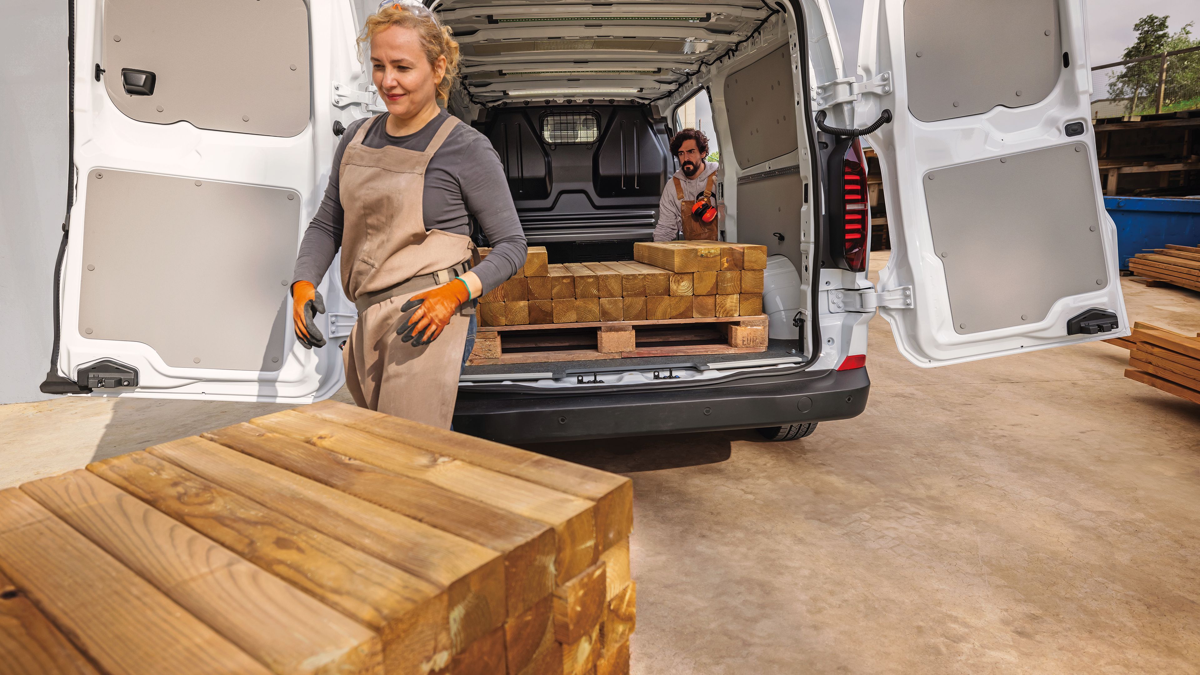 Задната част на Volkswagen e-Transporter с отворени врати и хора, които разтоварват дървен материал.