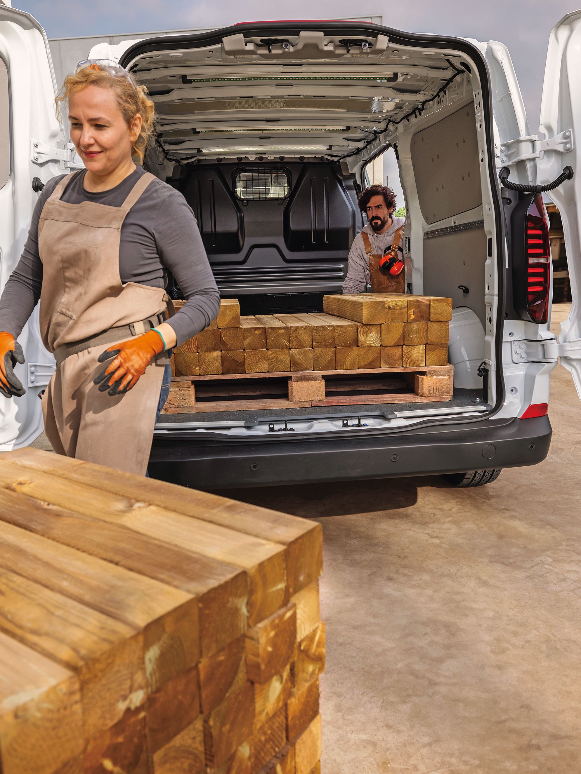 Задната част на Volkswagen e-Transporter с отворени врати и хора, които разтоварват дървен материал.