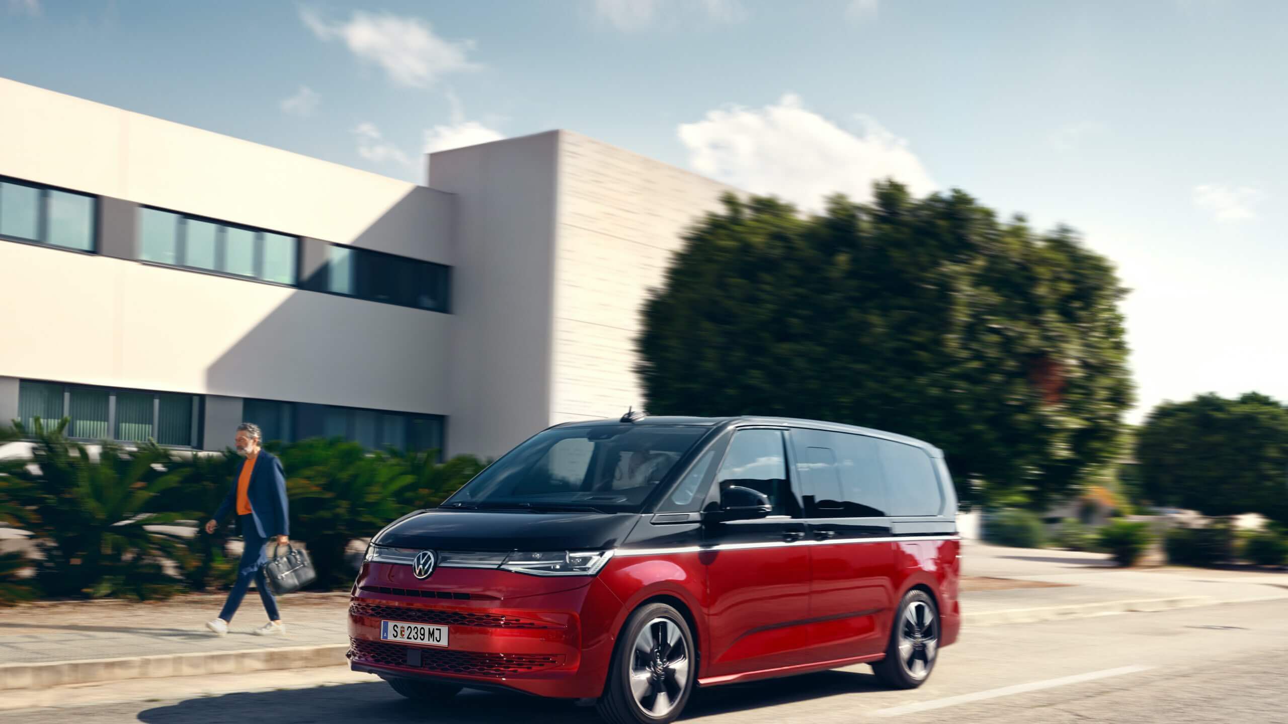 Der neue VW Multivan Style T7 fährt auf einer Straße neben einem Mann. 
