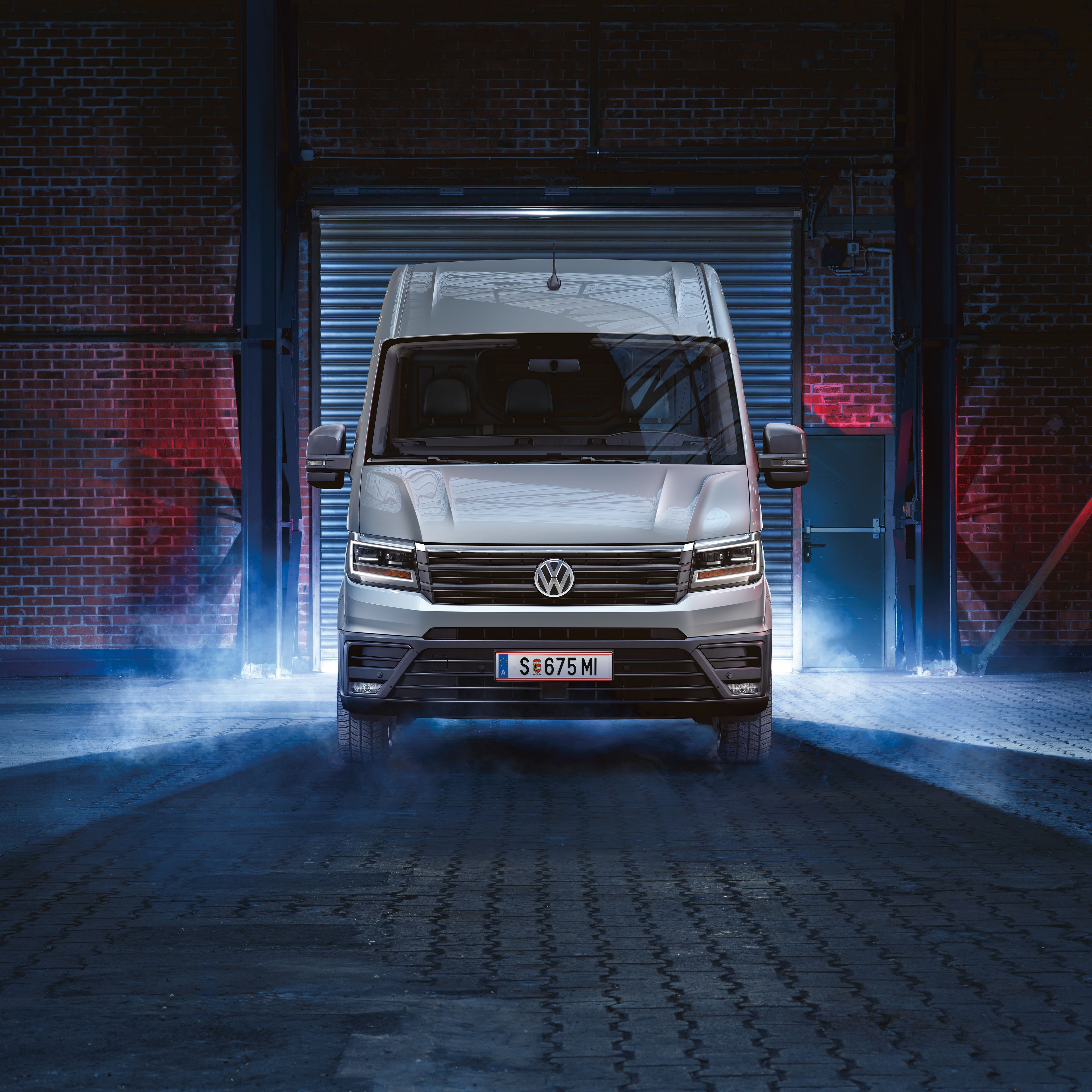 Volkswagen Crafter – създаден за професионалисти. Volkswagen Crafter в сребрист цвят излиза от складово хале с включени фарове.