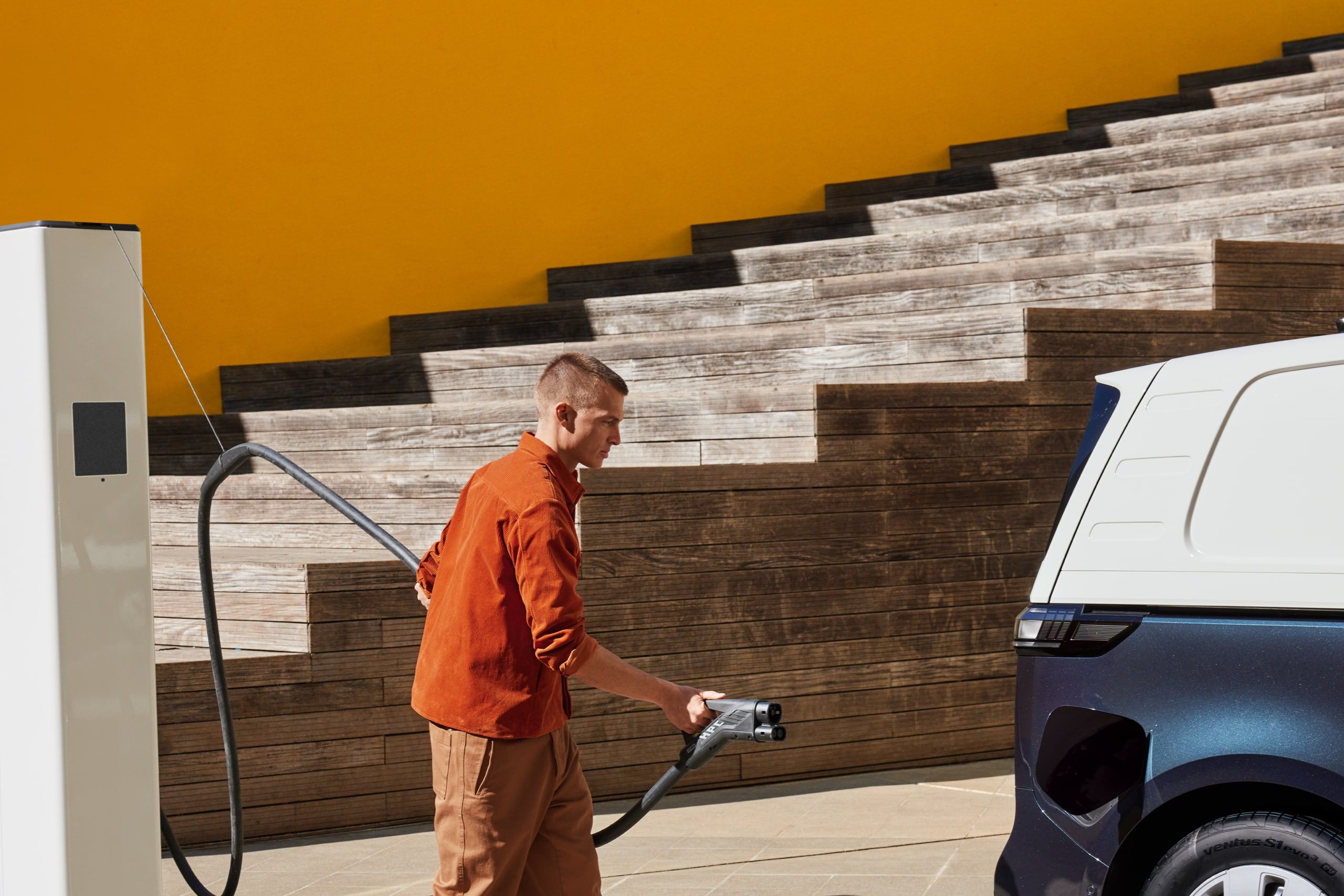 Мъж се подготвя да зареди електрически ван Volkswagen от зарядна станция.