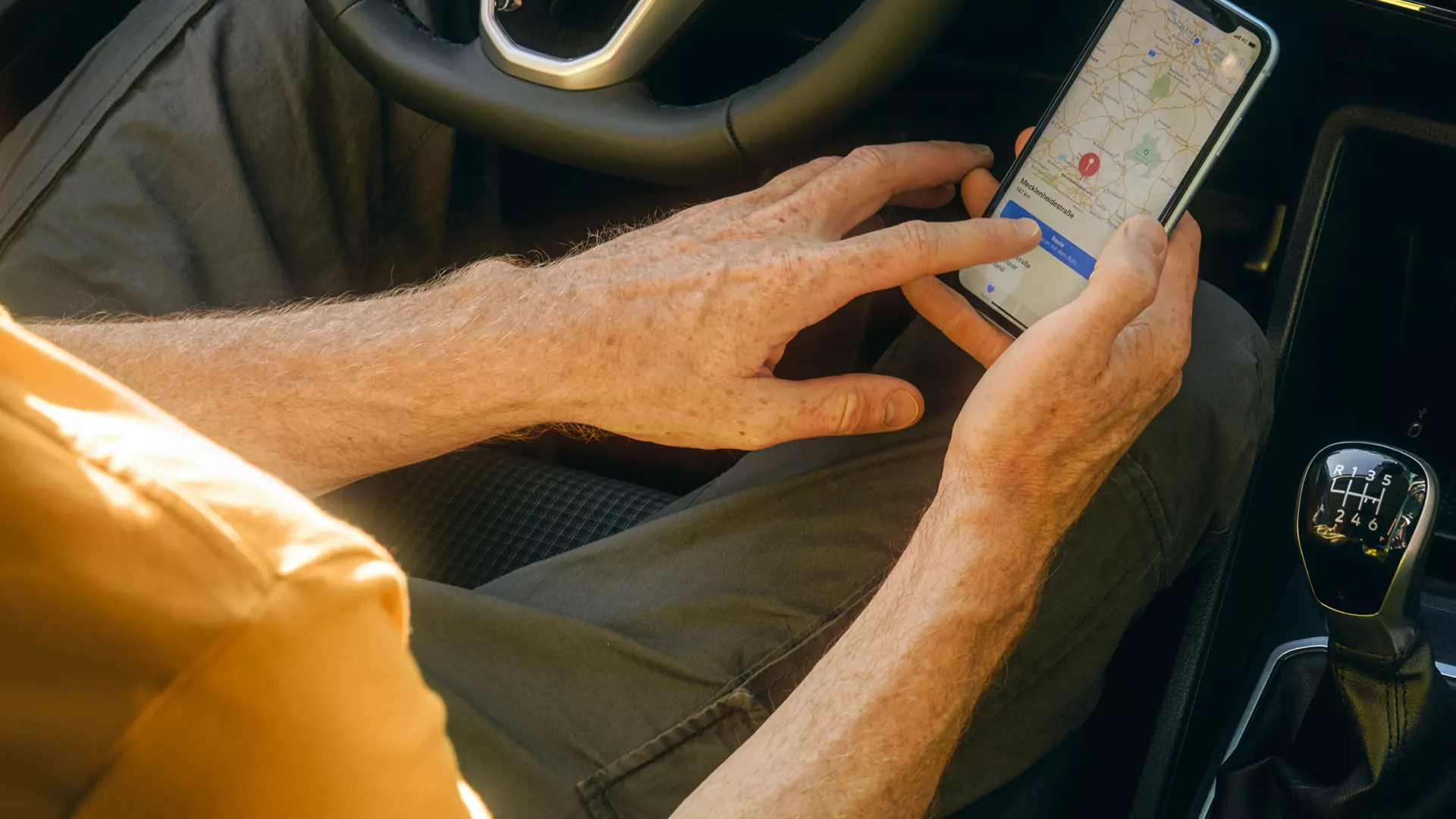 Куриер използва навигационно приложение на смартфон, седнал зад волана на автомобил Volkswagen с дигитален кокпит и модерен мултимедиен екран.