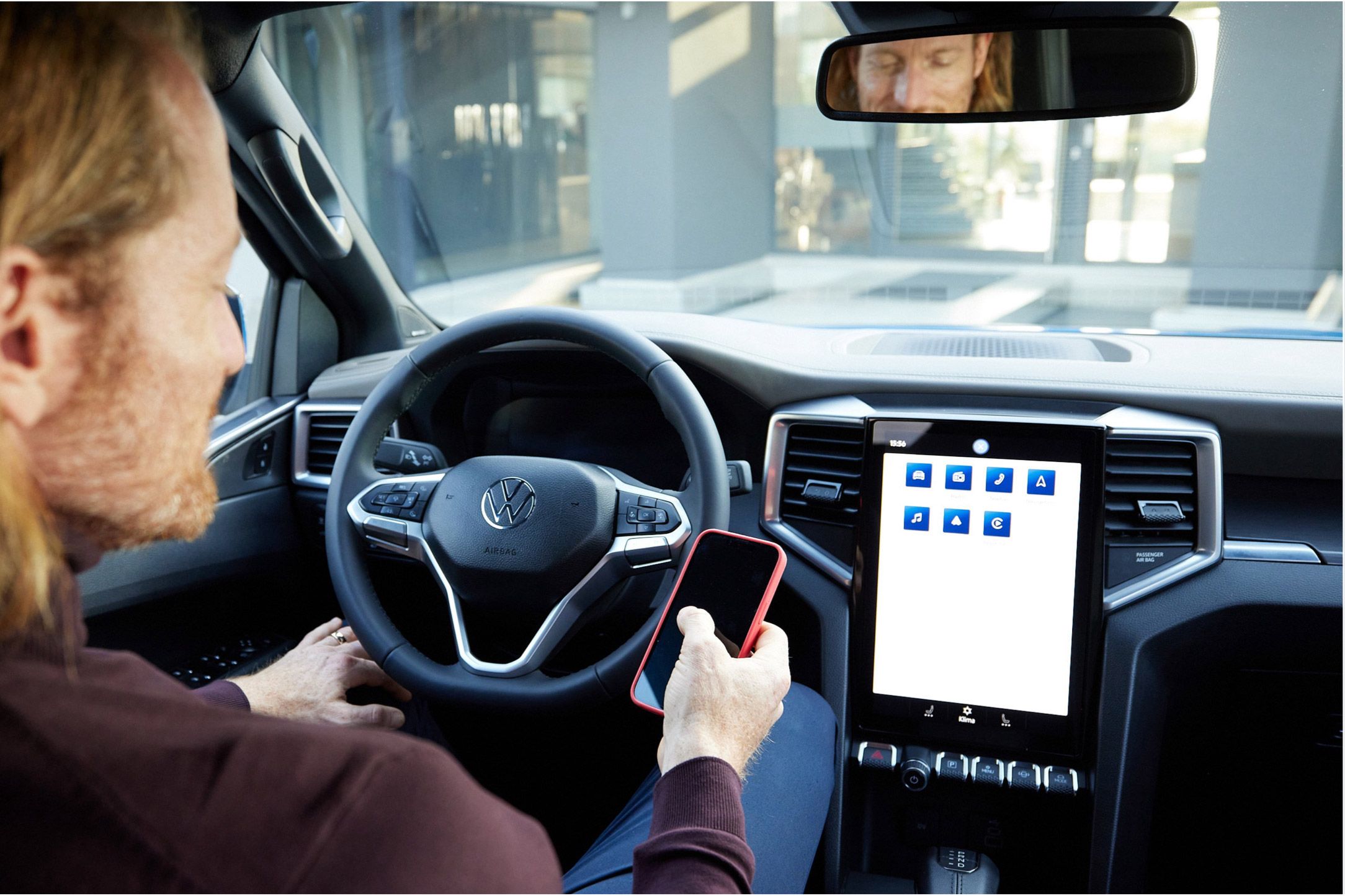 Мъж в купето на Volkswagen използва смартфон, свързан с централния дисплей на автомобила