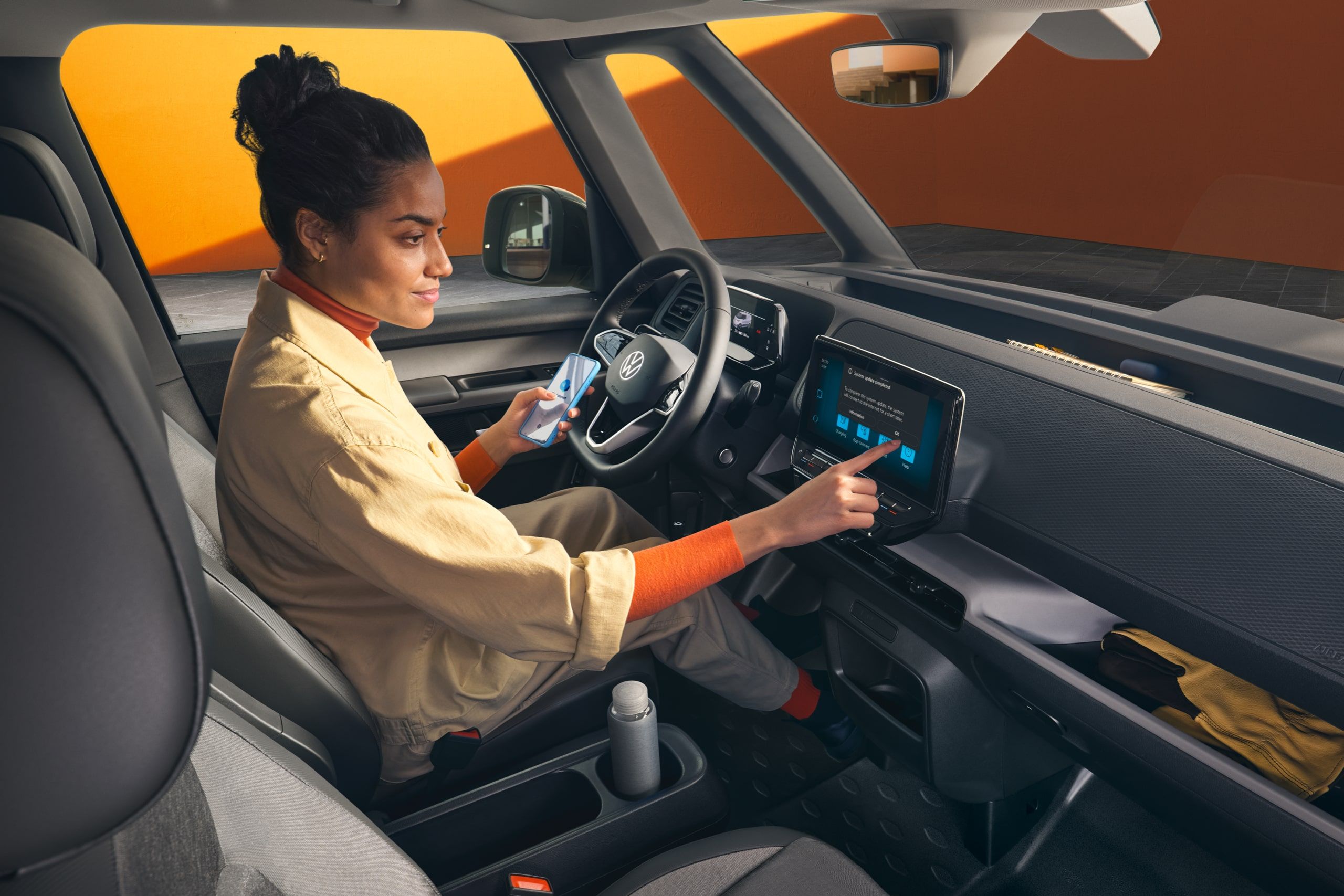 Жена използва инфотейнмънт системата на Volkswagen ID. Buzz Cargo, докато държи смартфон