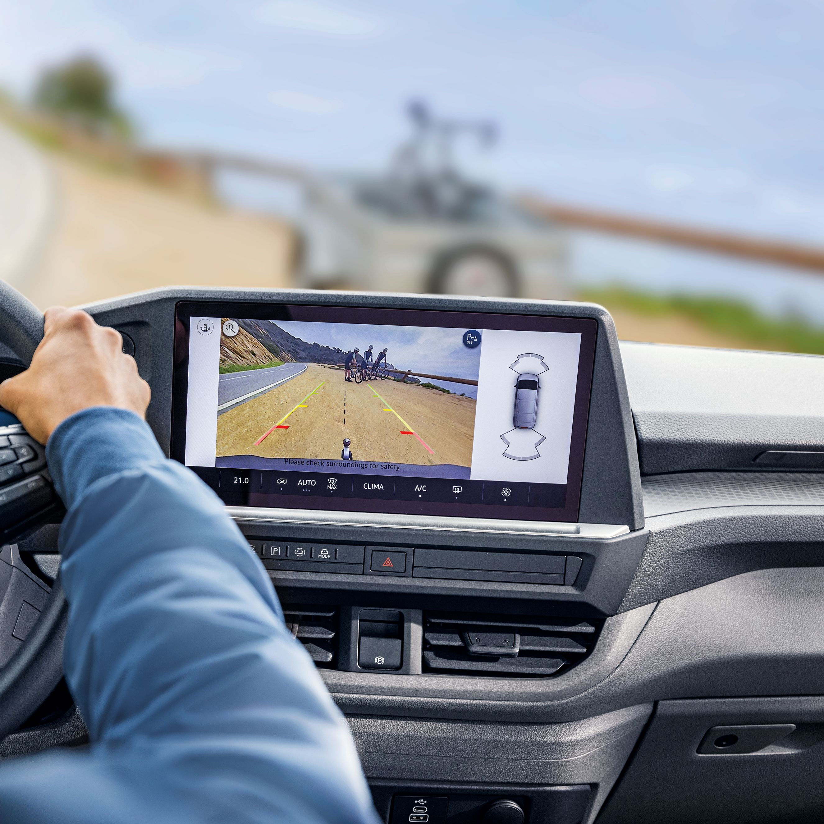 Водач управлява Volkswagen Caravelle с активирана камера за задно виждане и асистент при паркиране с ремарке