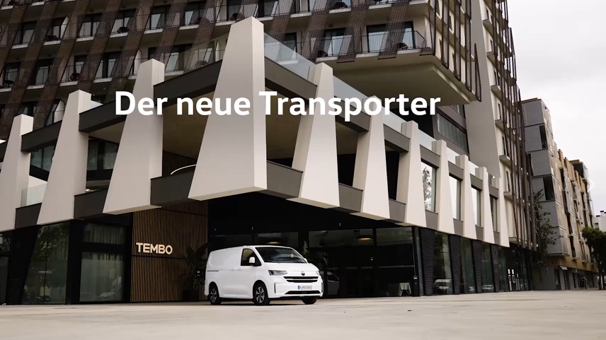 Бял Volkswagen Transporter, паркиран пред модерен хотел TEMBO с надпис „Der neue Transporter“