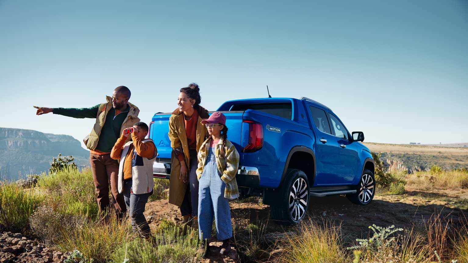 Eine Familie parkt mit einem blauen Amarok in den Bergen und blickt in die Ferne