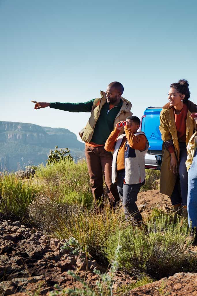 Eine Familie parkt mit einem blauen Amarok in den Bergen und blickt in die Ferne