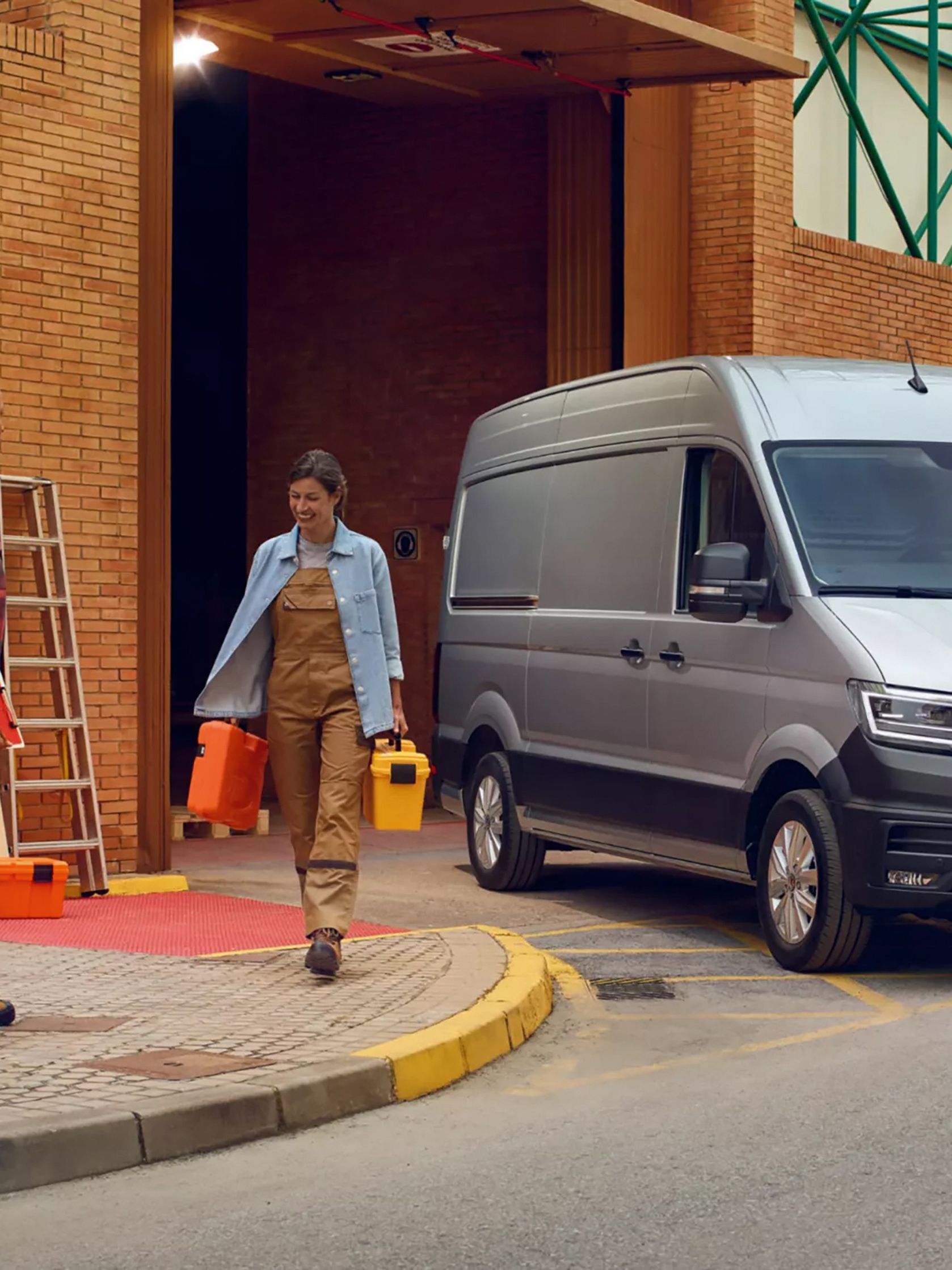 Der neue Crafter Двама работници пред сграда със сив Volkswagen Crafter, паркиран на товарна рампа.