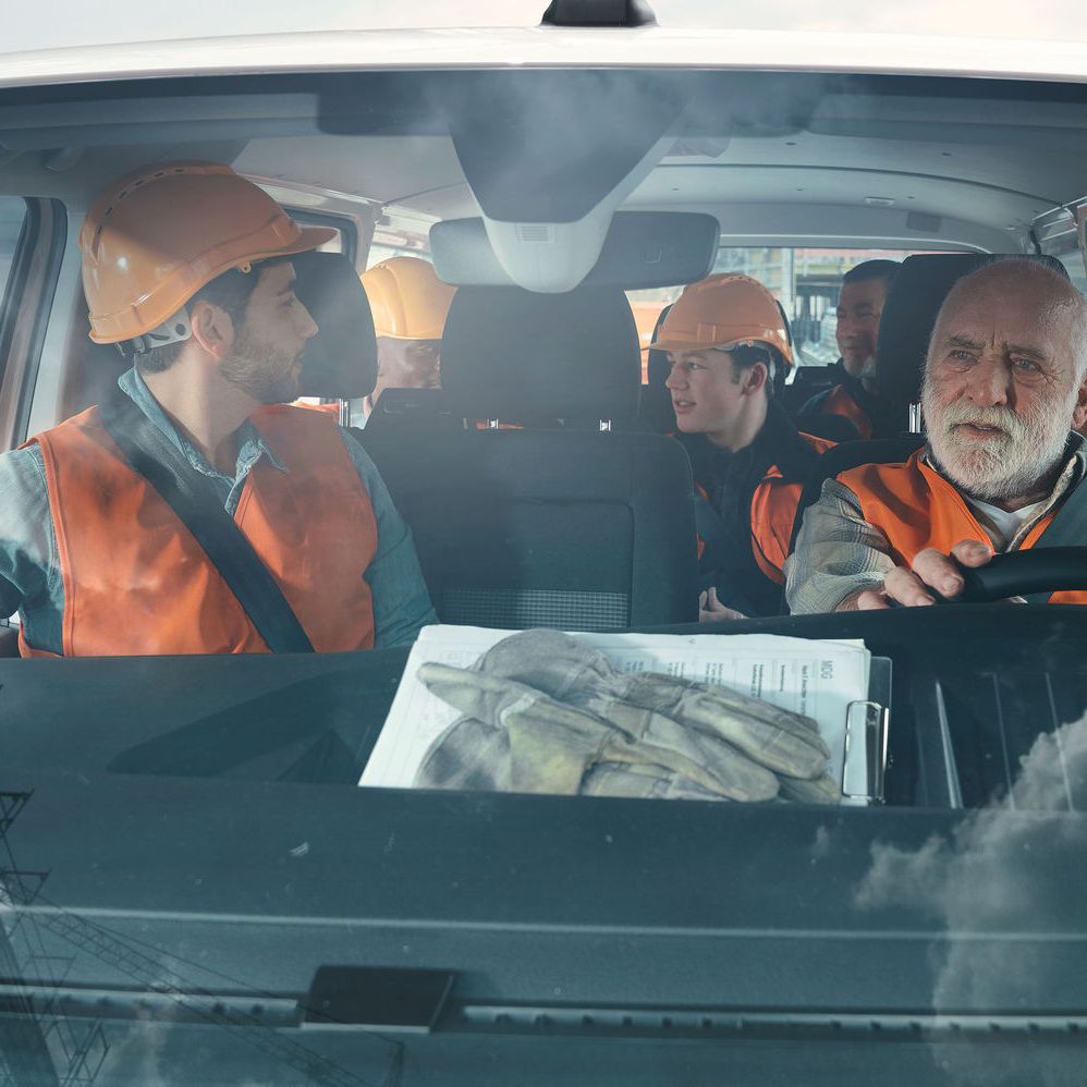 Просторен Volkswagen ван за екипна работа Работници с каски и светлоотразителни жилетки пътуват във Volkswagen ван, заснети през предното стъкло