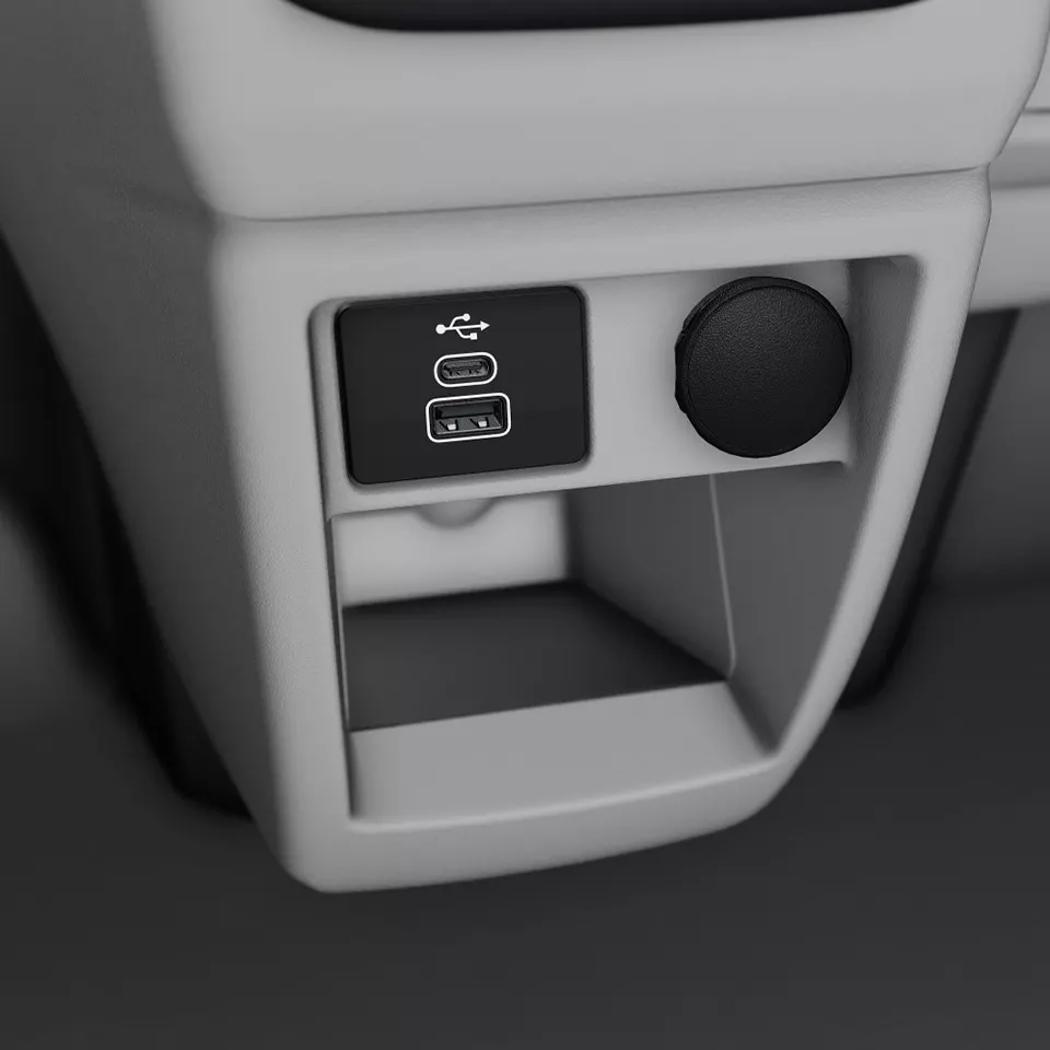Снимката показва вътрешността на автомобил с USB портове и компактен кръгъл бутон за свързване на електрически устройства. Бутоните са разположени върху панел близо до централната конзола. Под тях има малко отделение за съхранение.