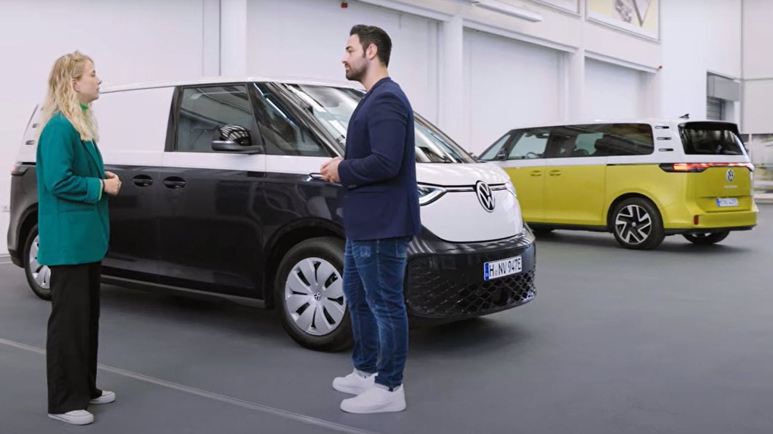 Двама души разговарят пред Volkswagen ID. Buzz Cargo в изложбена зала, с още един ID. Buzz на заден план.