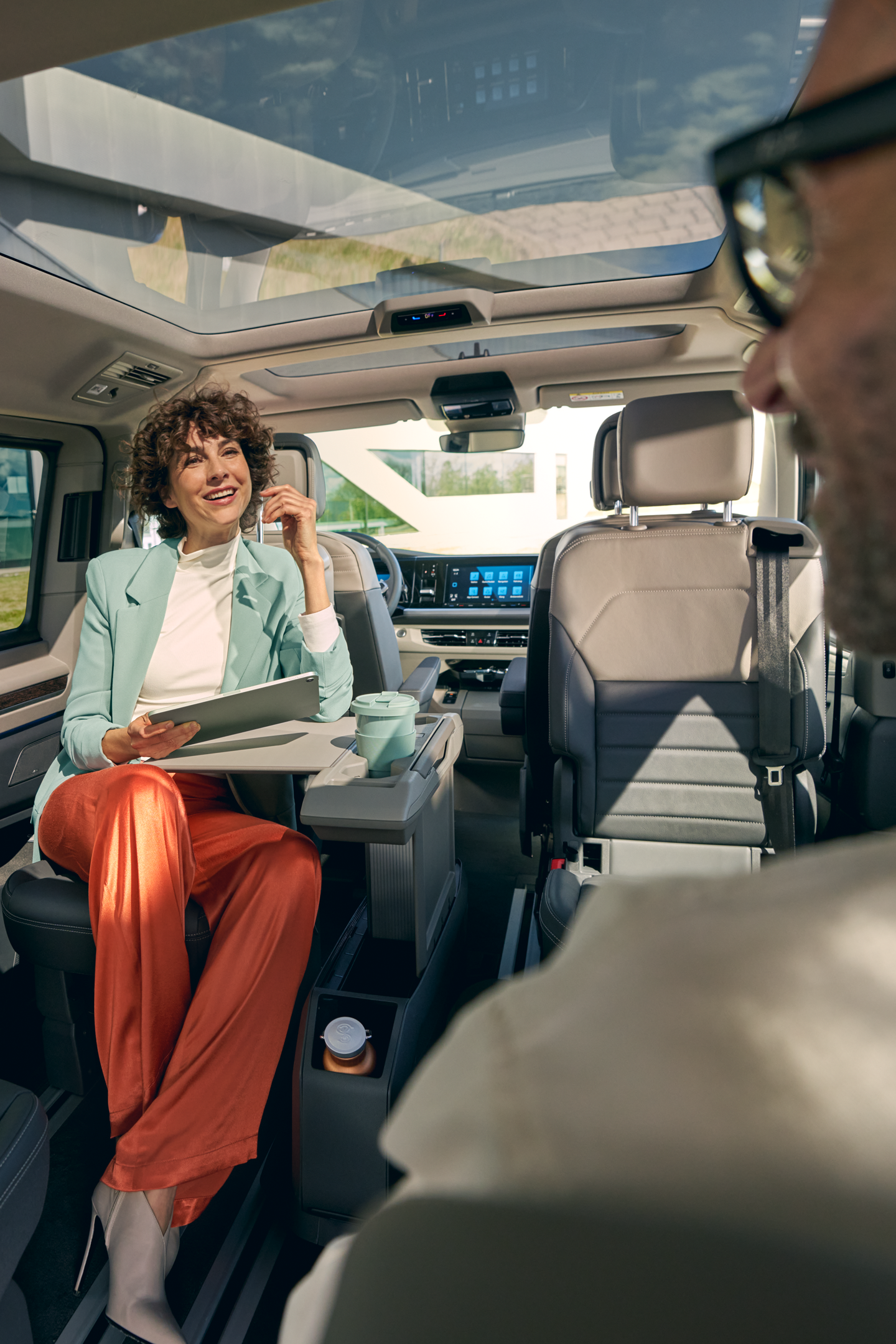 Просторен и модерен интериор на Volkswagen Multivan Жена с таблет разговаря с мъж в просторния интериор на Volkswagen Multivan с панорамен покрив.