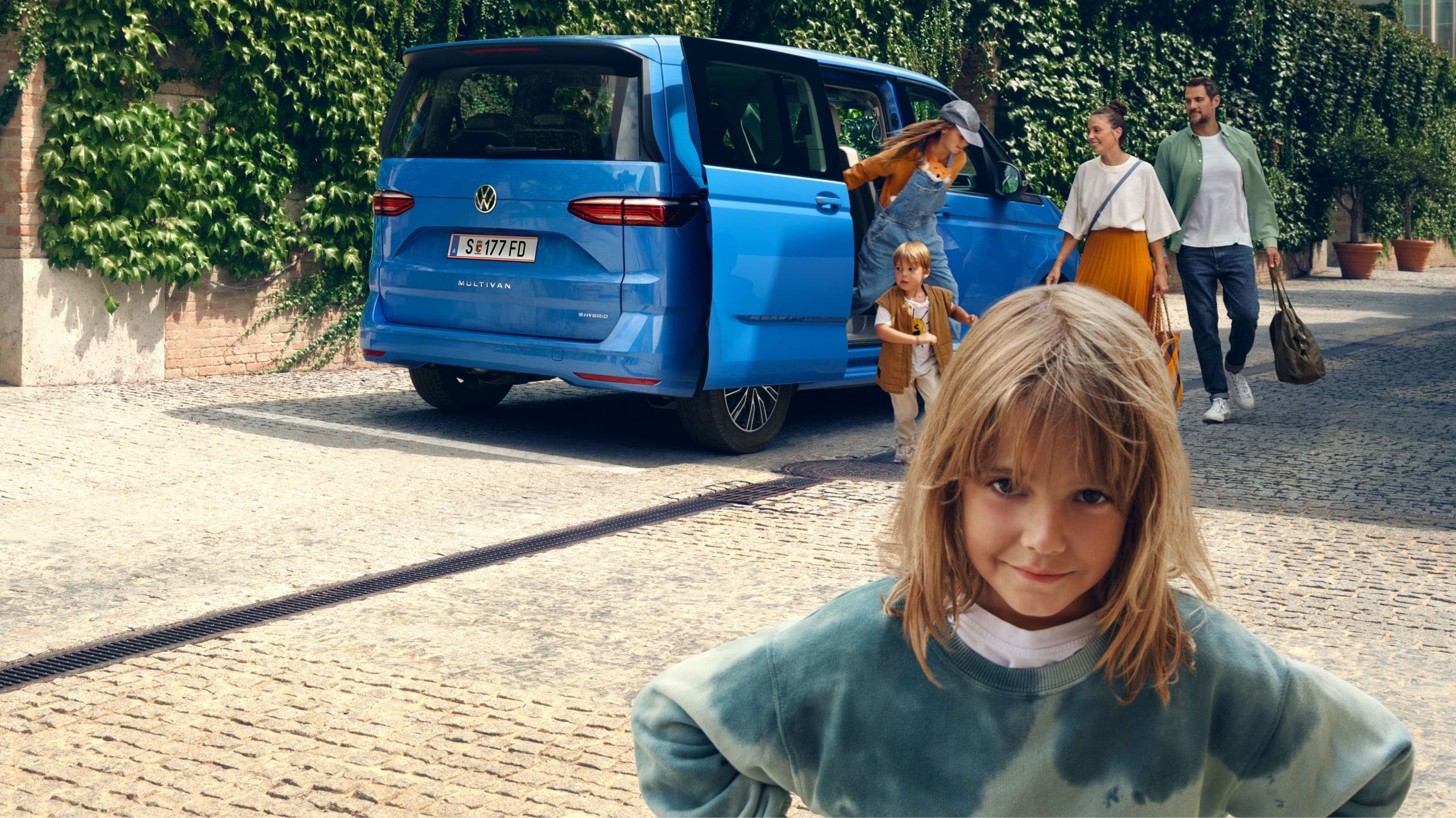 Ein Mädchen steht vor dem neuen VW Multivan T7 2021 und schaut trotzig in die Kamera.