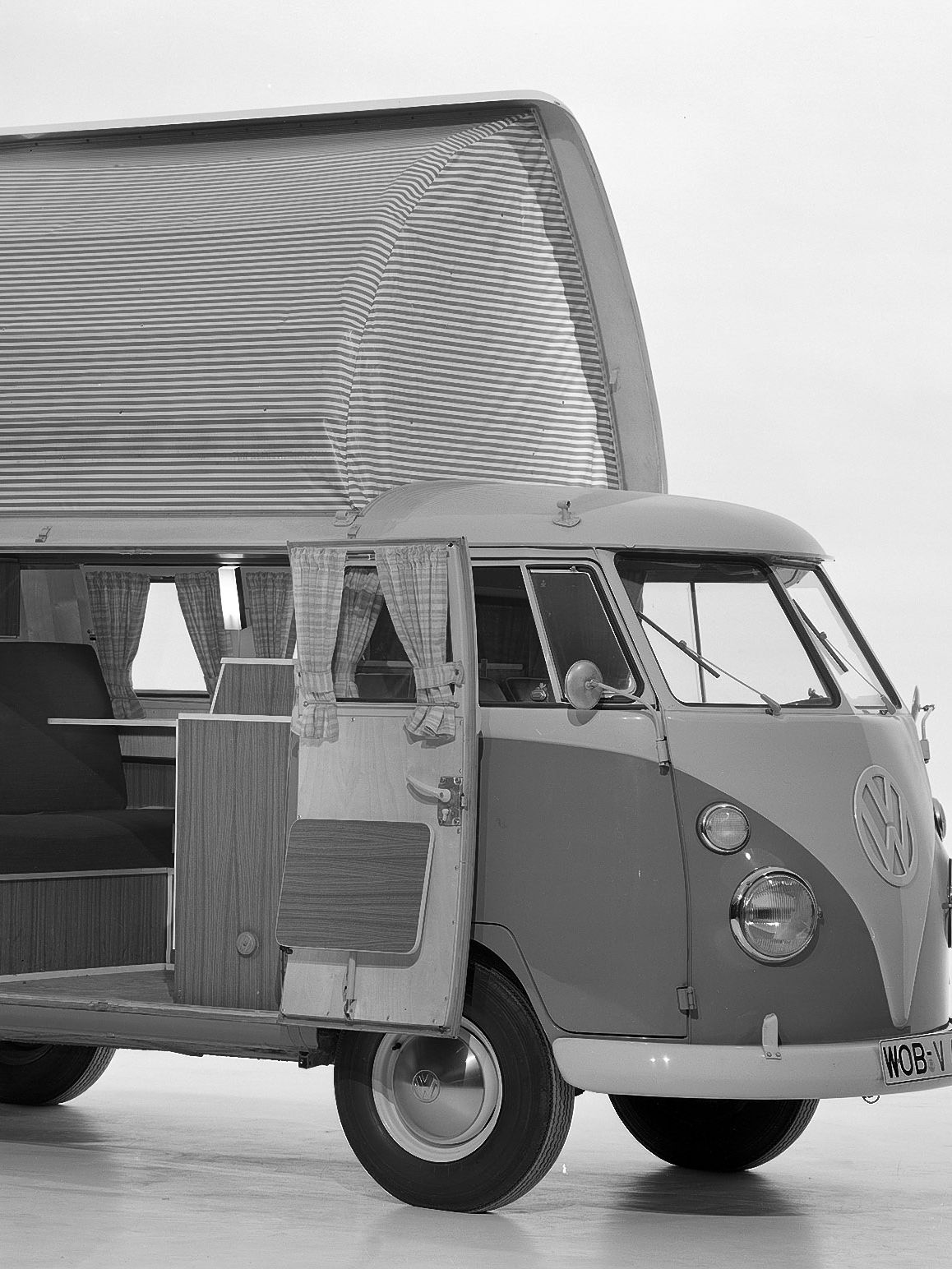 Черно-бяла снимка на Volkswagen Transporter T1 Westfalia Camper с отворени врати и повдигащ се покрив.