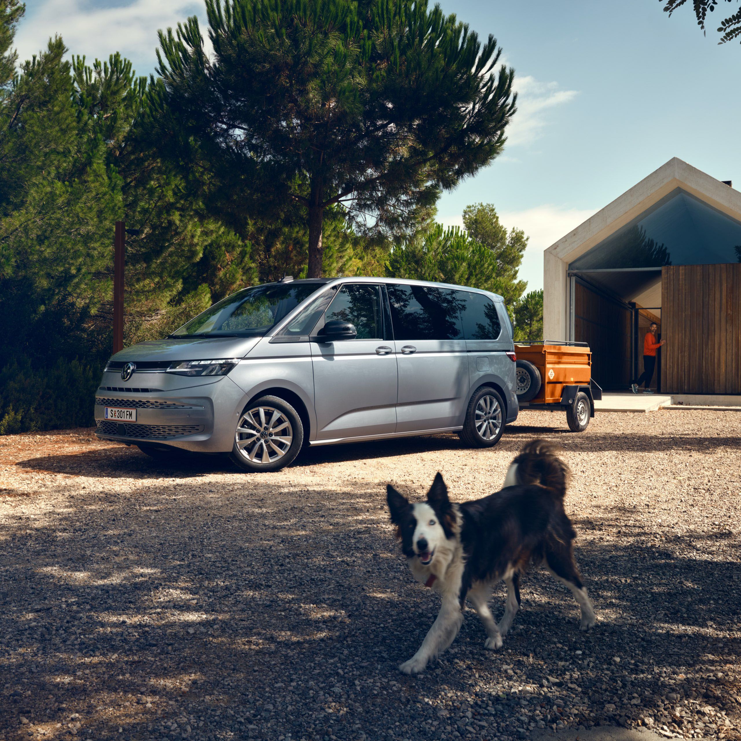 Der neue VW T7 Multivan in Silber steht vor Scheune und Hund lauft vorbei