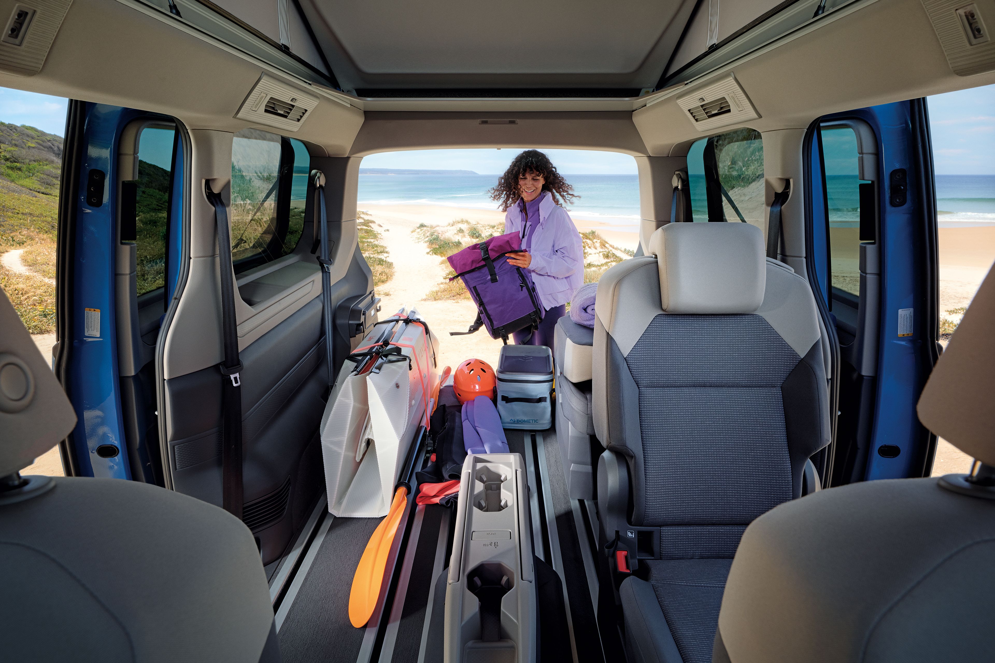 Жена подготвя оборудване за сърф до Volkswagen California, паркиран на плажа.