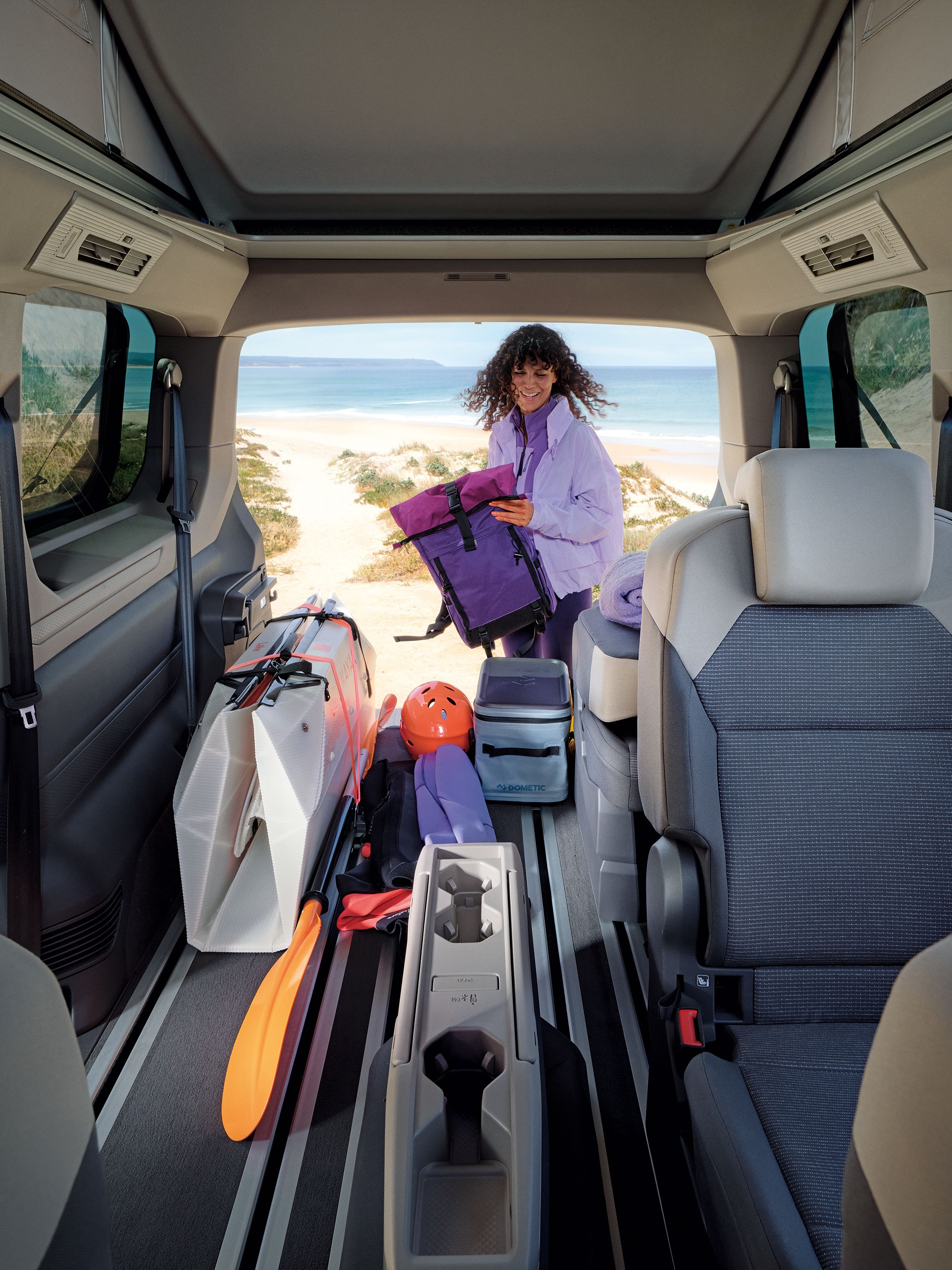 Жена подготвя оборудване за сърф до Volkswagen California, паркиран на плажа.