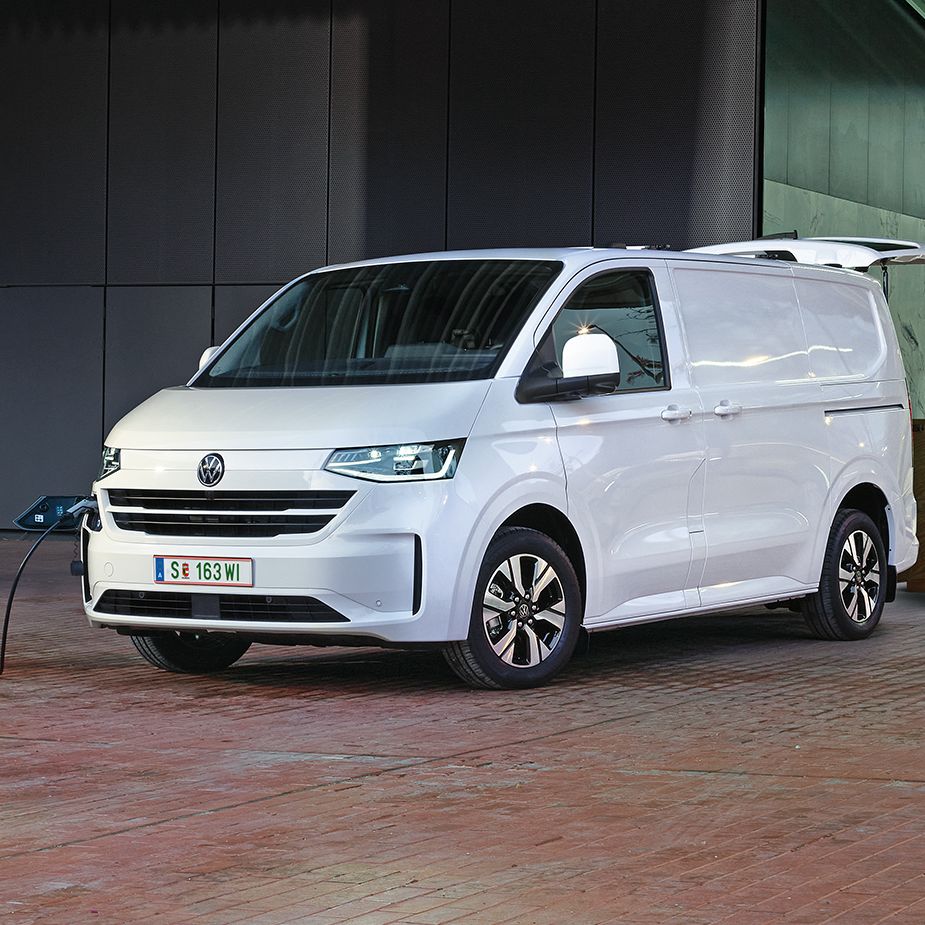 Електрически Volkswagen Transporter, включен към зарядна станция пред офис сграда, докато се разтоварват стоки.
