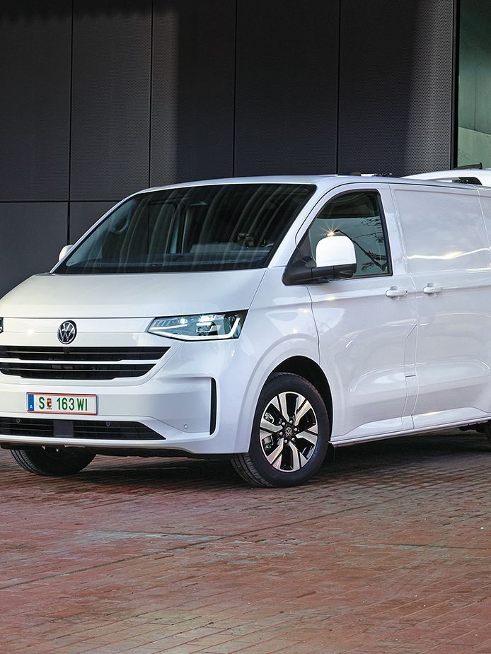 Електрически Volkswagen Transporter, включен към зарядна станция пред офис сграда, докато се разтоварват стоки.