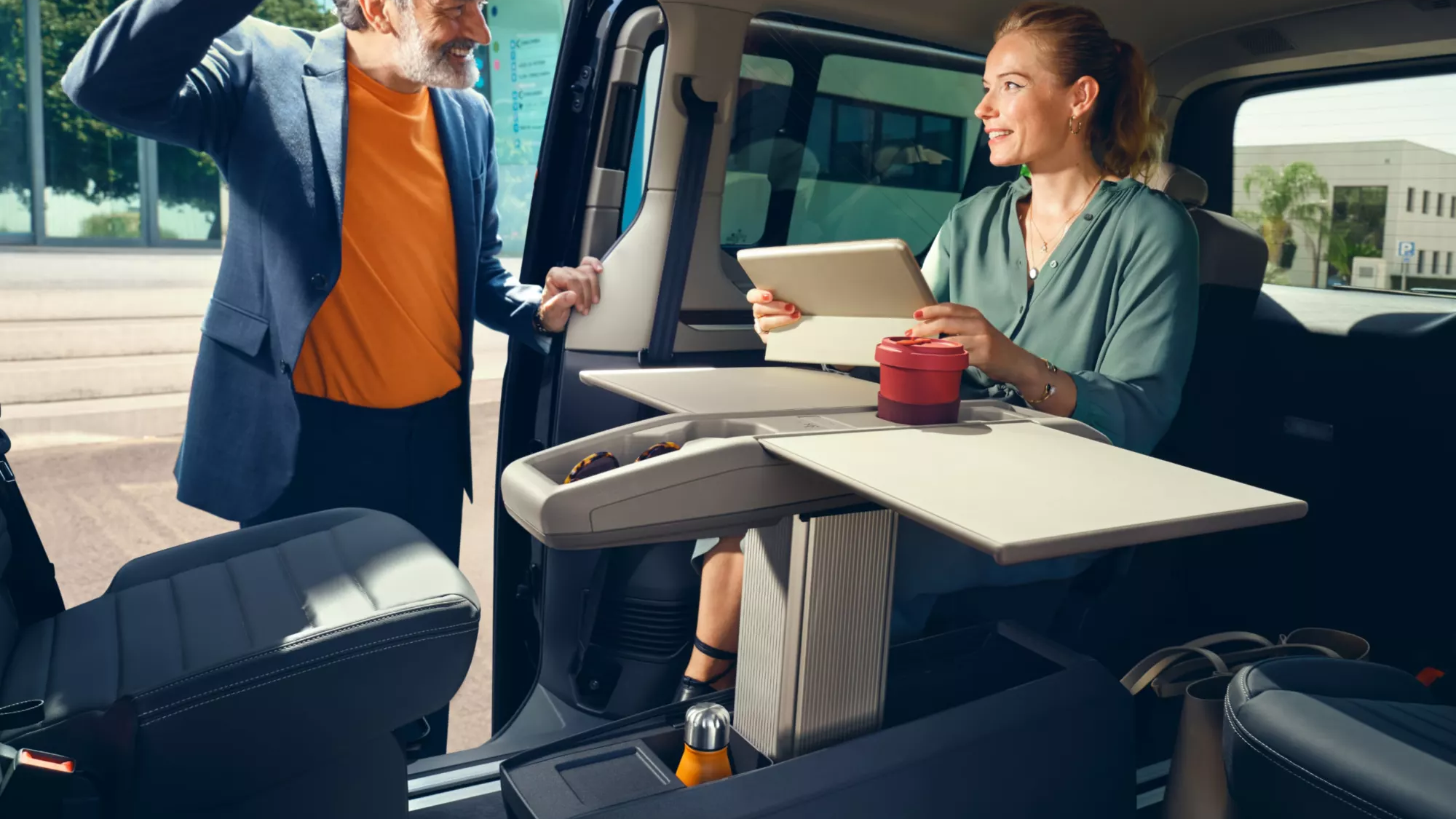 Mann öffnet Schiebetüre des neuen Multivans, Frau sitzt im Fahrgastraum