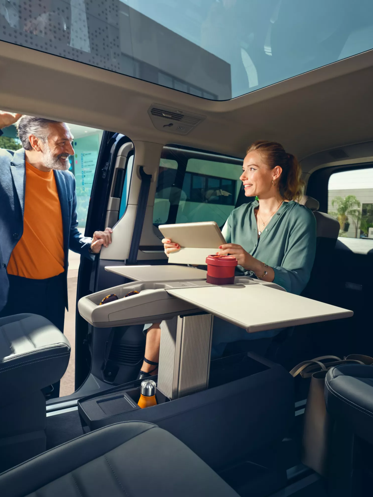 Mann öffnet Schiebetüre des neuen Multivans, Frau sitzt im Fahrgastraum