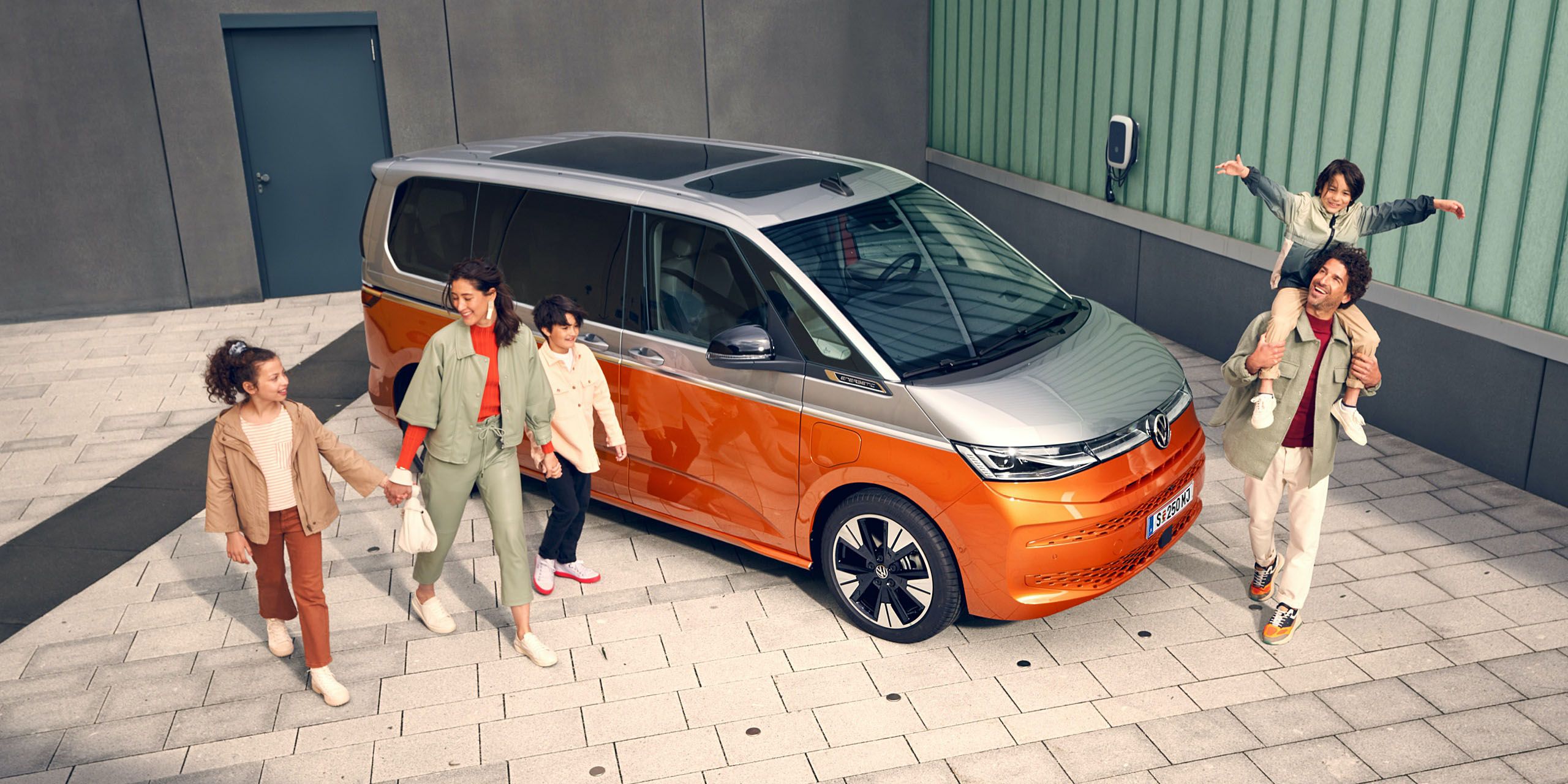 Eine Familie läuft vergnügt neben dem stehenden VW Multivan Energetic T7 2021 her
