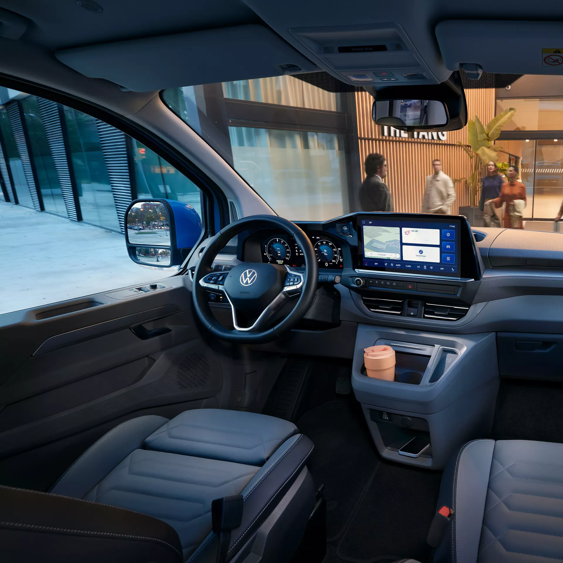 Интериор на Volkswagen Caravelle с модерен кокпит и дигитален дисплей, паркиран пред хотел