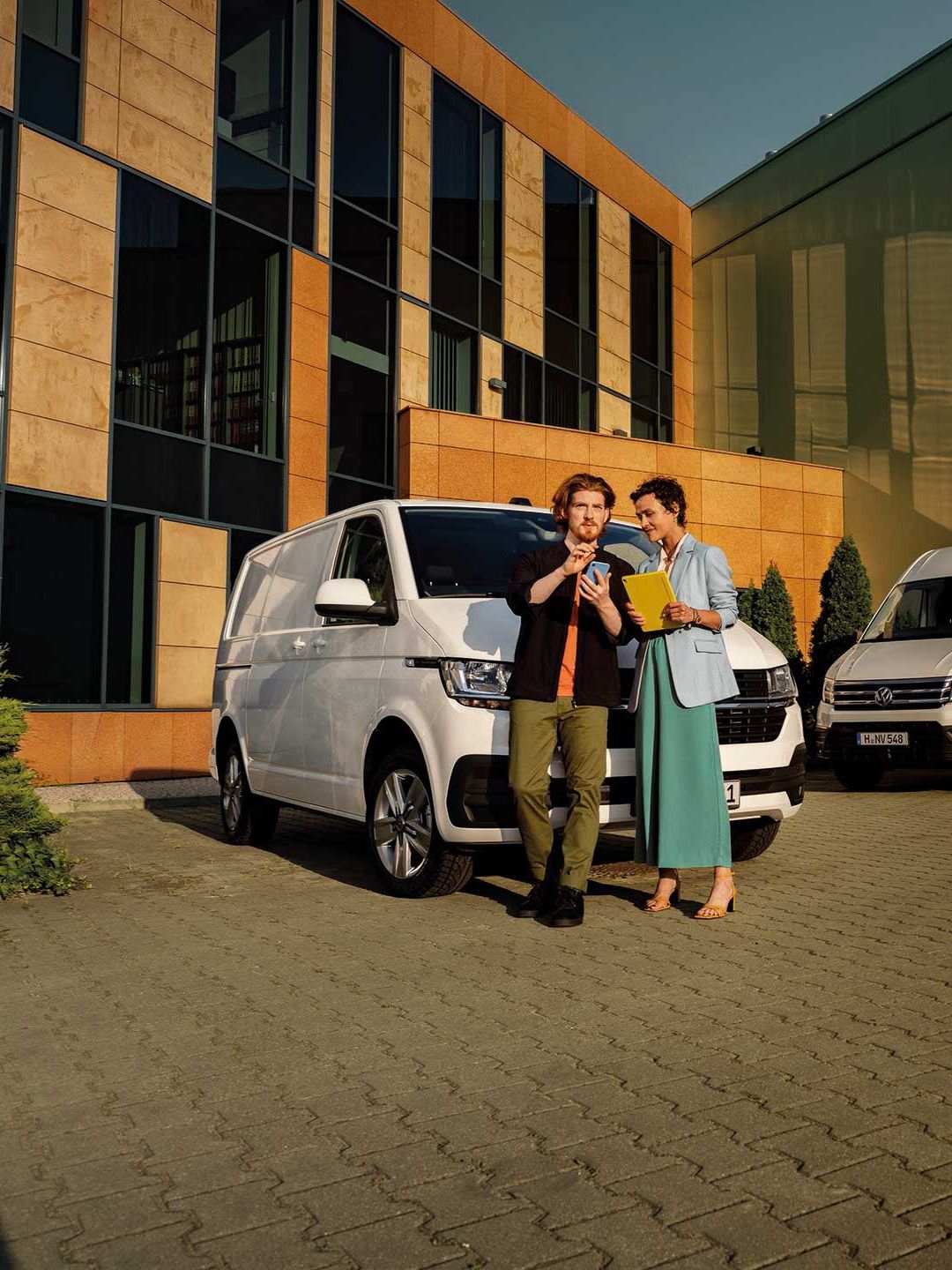 Мъж и жена разговарят пред спряни VW лекотоварни автомобили