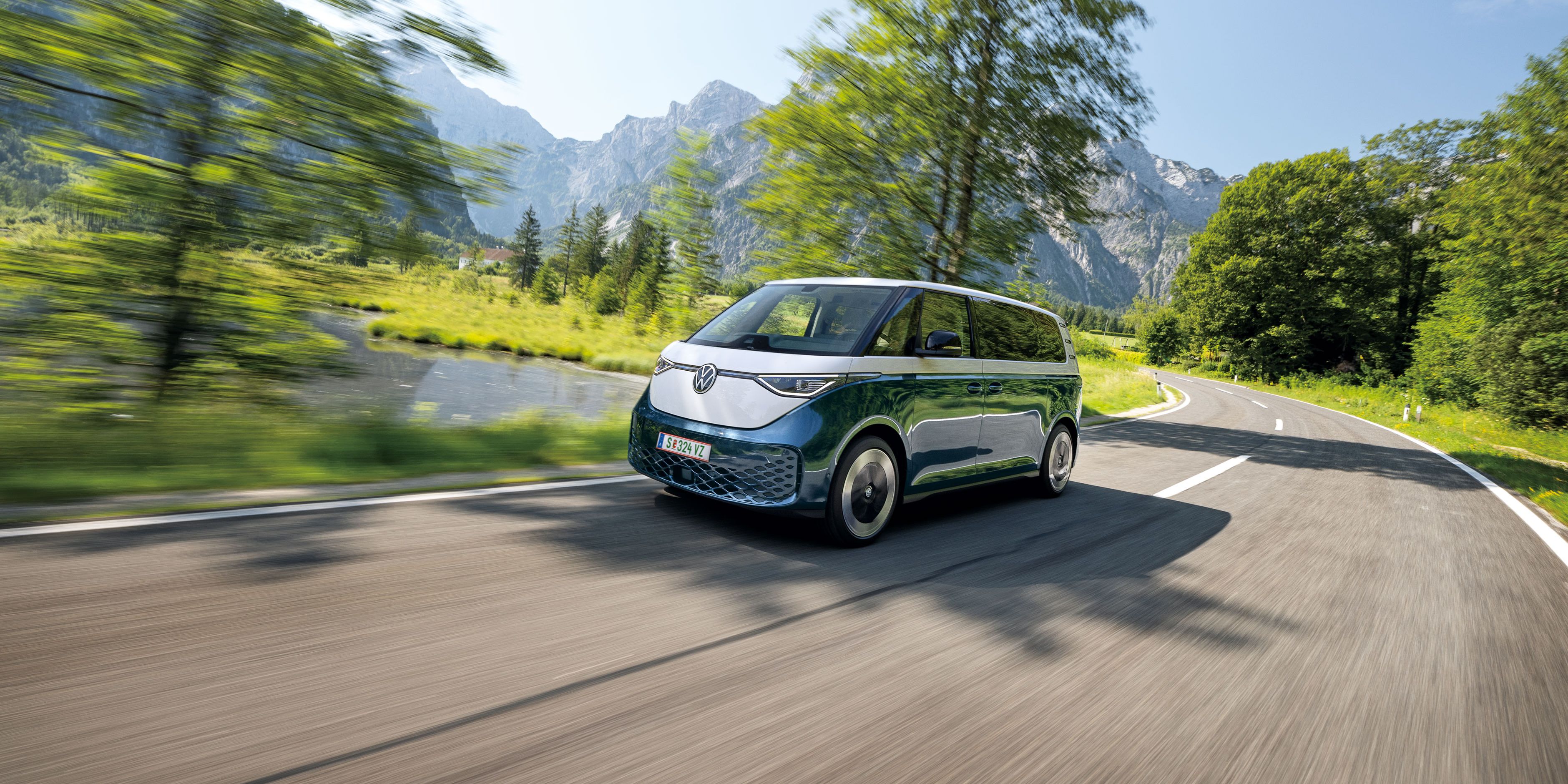 Електрическият Volkswagen ID. Buzz в движение сред живописен планински пейзаж с езеро и скалисти върхове.