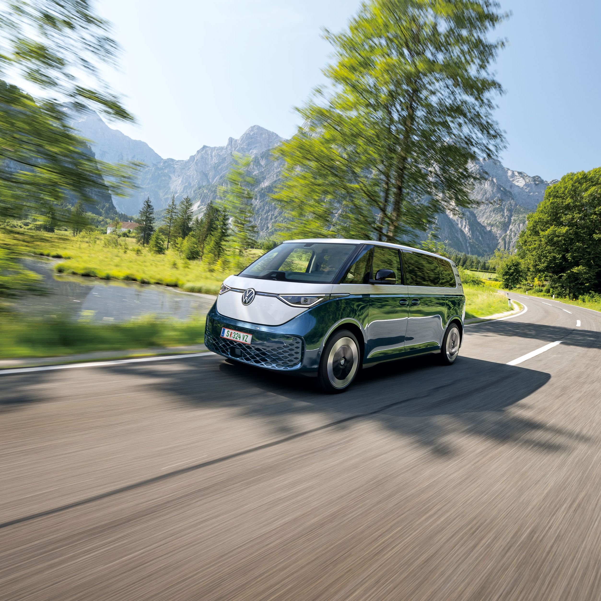 Електрическият Volkswagen ID. Buzz в движение сред живописен планински пейзаж с езеро и скалисти върхове.
