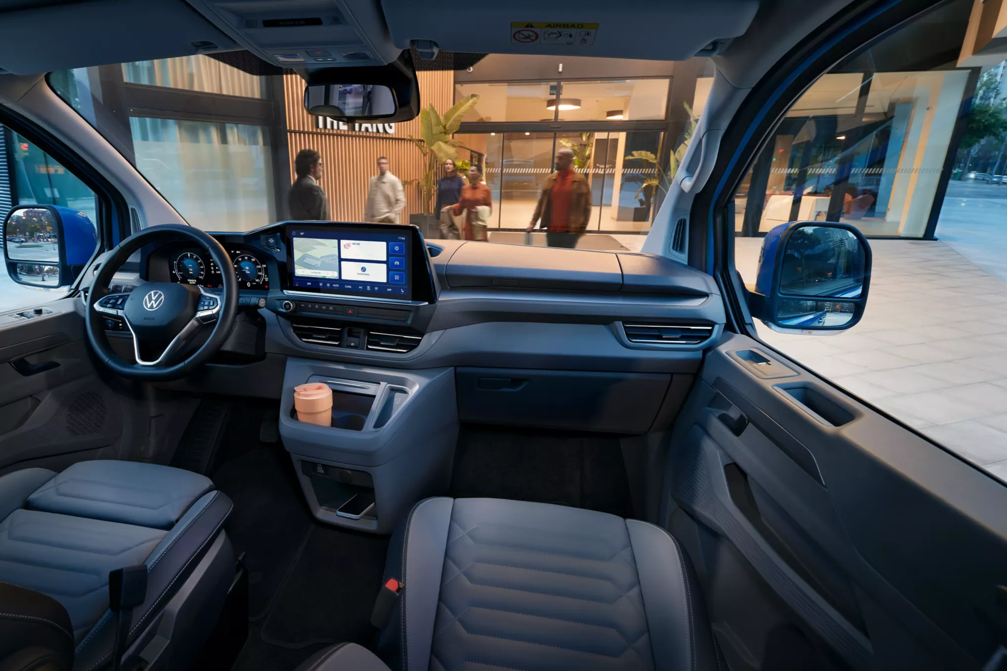 Интериор на Volkswagen Caravelle с модерен кокпит и дигитален дисплей, паркиран пред хотел