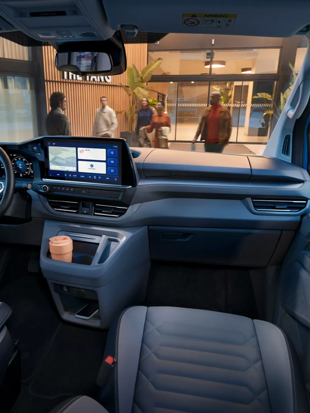 Интериор на Volkswagen Caravelle с модерен кокпит и дигитален дисплей, паркиран пред хотел